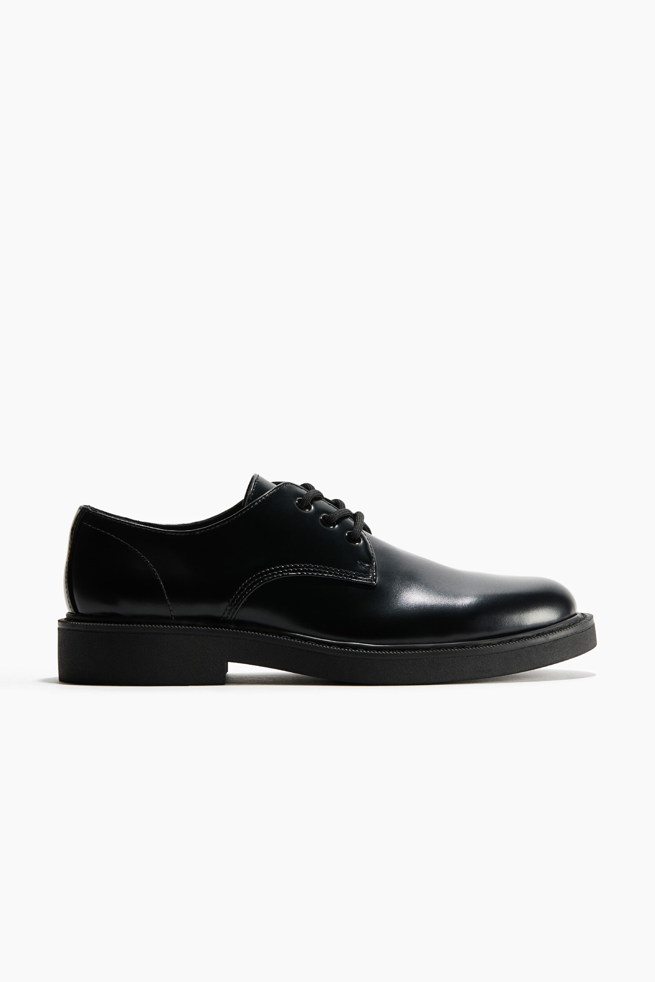 View larger image: A black leather derby shoe is shown in side profile, showcasing a polished upper, a rounded toe, and a three-eyelet lace-up closure. The shoe rests on a thick black rubber sole with a low block heel.