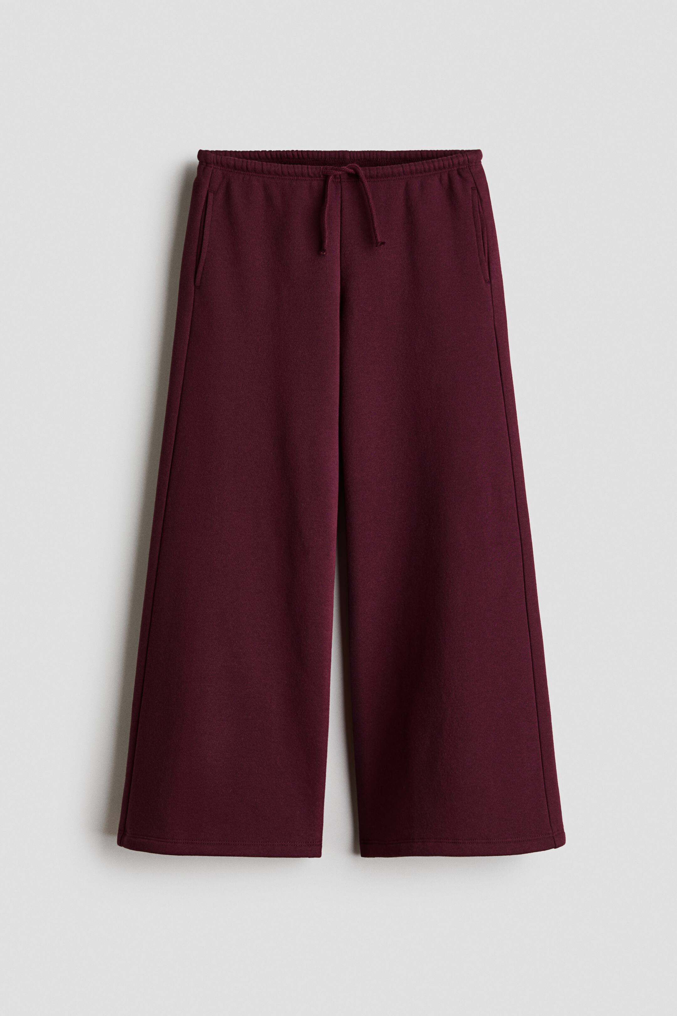 View larger image: Burgundy joggers in a sweatshirt fabric are lying flat, viewed from the front, featuring an elasticated drawstring waist, discreet side pockets, and straight, wide legs.