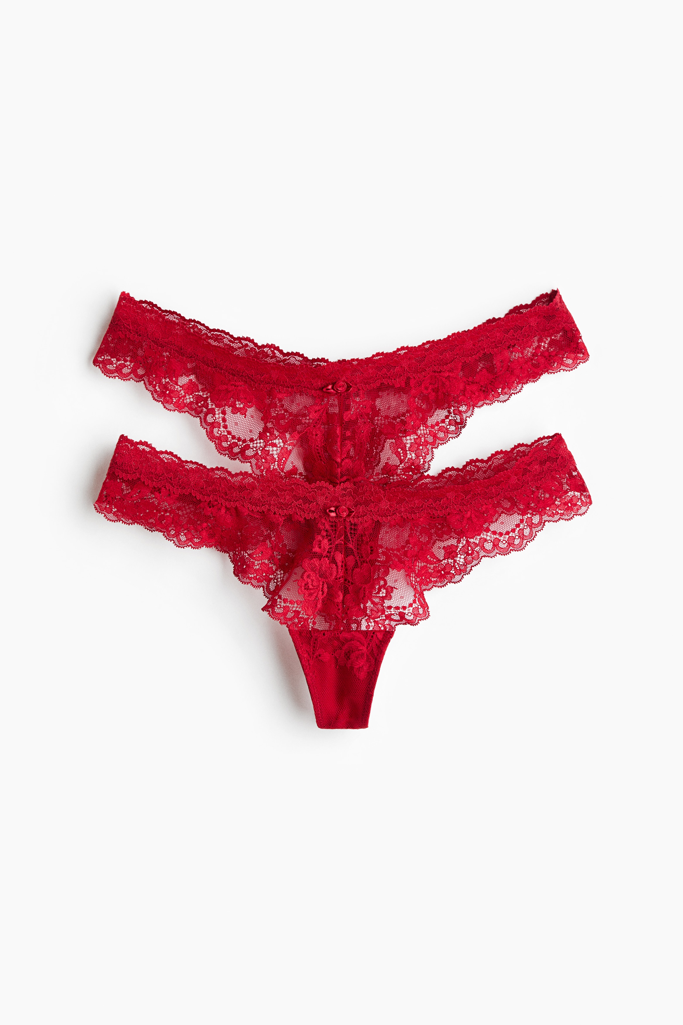 Lace G-strings in a bright pink colour are being worn by the model, featuring a low-rise waist with scalloped edges and a decorative centre bow. The product is being paired with a matching lace underwire bra.