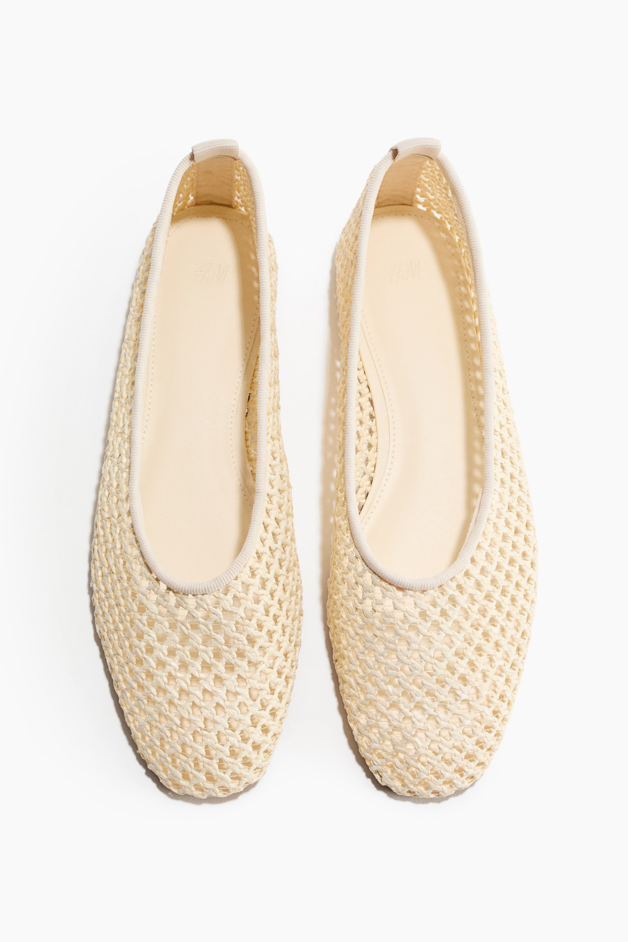 View larger image: A pair of light beige flats features a woven, mesh-like upper and a rounded toe, shown from the front. Each shoe features an elastic ribbed trim along the opening and a smooth, lighter beige insole.