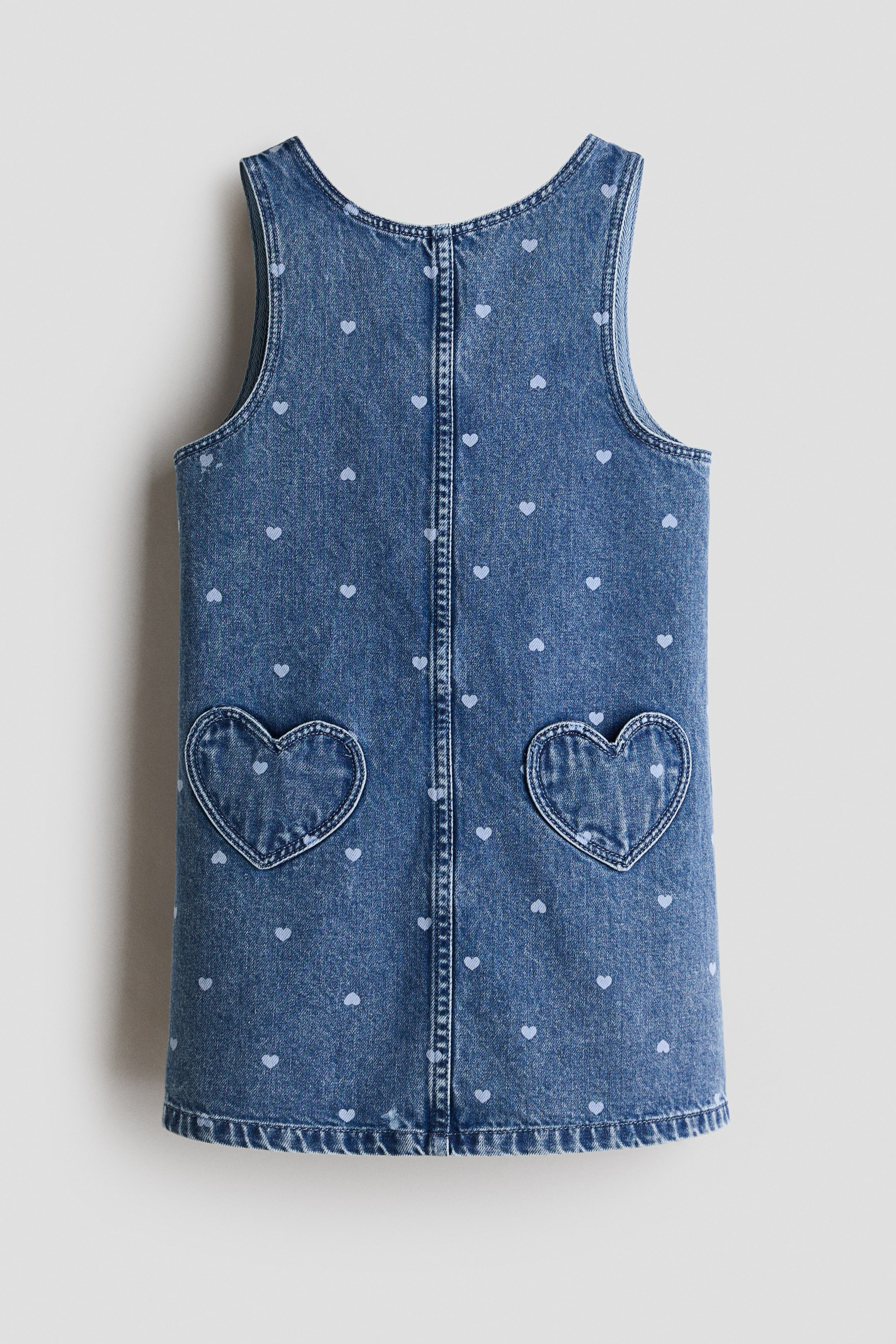 View larger image: A blue denim sleeveless dress showcases its back view, adorned with an all-over pattern of small light blue hearts. Two heart-shaped patch pockets are placed on the lower back, and a vertical seam runs down the center.