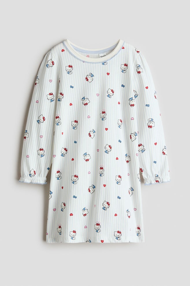 Une chemise de nuit présente une base blanche avec des rayures verticales bleu clair et un imprimé répété de personnages Hello Kitty, de cœurs rouges et de nœuds bleus. Elle arbore un col rond avec une bordure blanche et une bande intérieure bleu clair, accentuée par des coutures bleues sur la bordure extérieure. Les manches longues sont froncées aux poignets avec des coutures froncées bleues. - 1