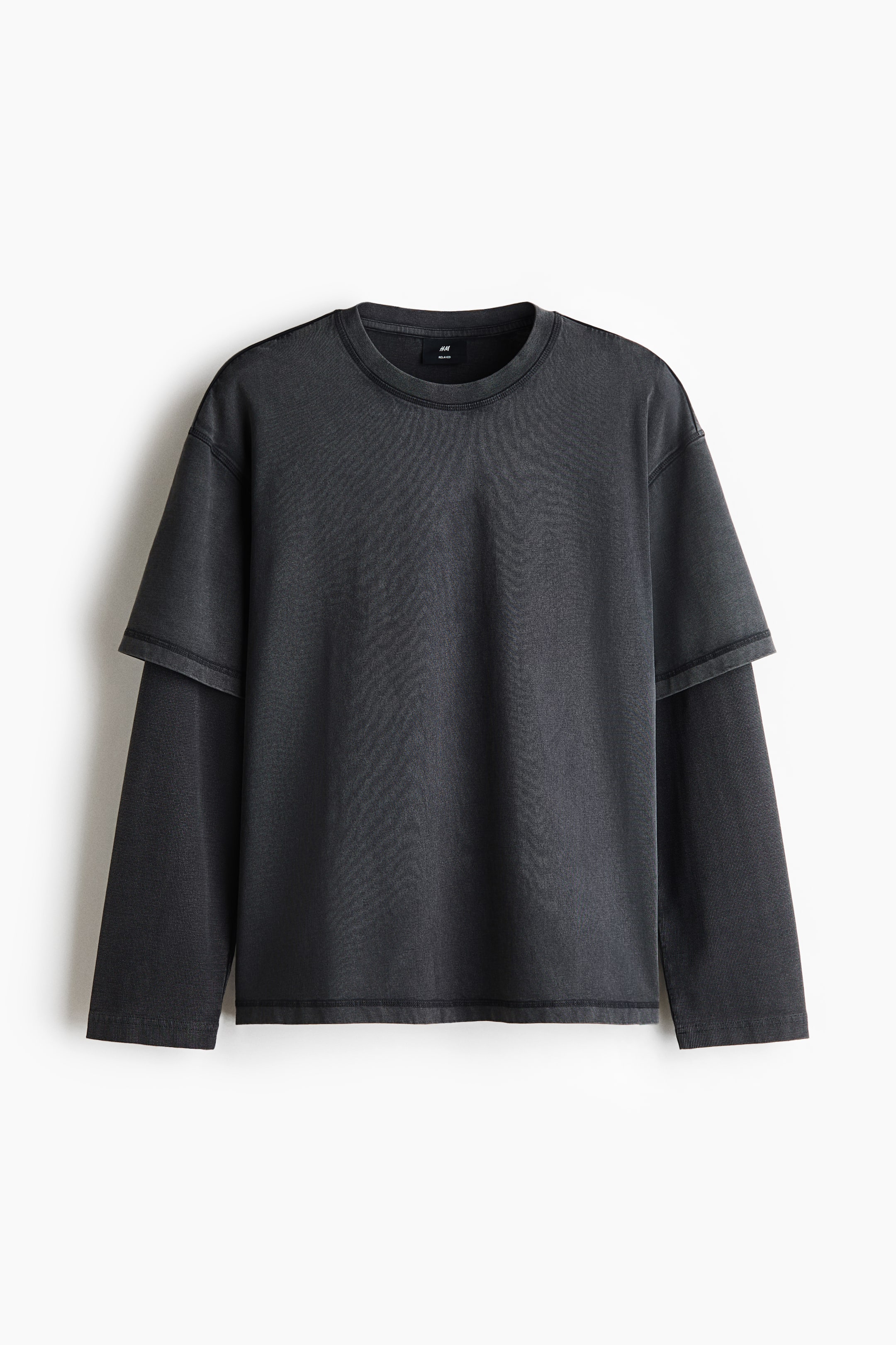 View larger image: A dark grey, heavyweight cotton jersey tee is hanging in a front-facing view, displaying a layered design with long sleeves sewn underneath short, dropped-shoulder sleeves. The relaxed-fit garment features a ribbed round neckline and a straight-cut hem with a faded wash finish.