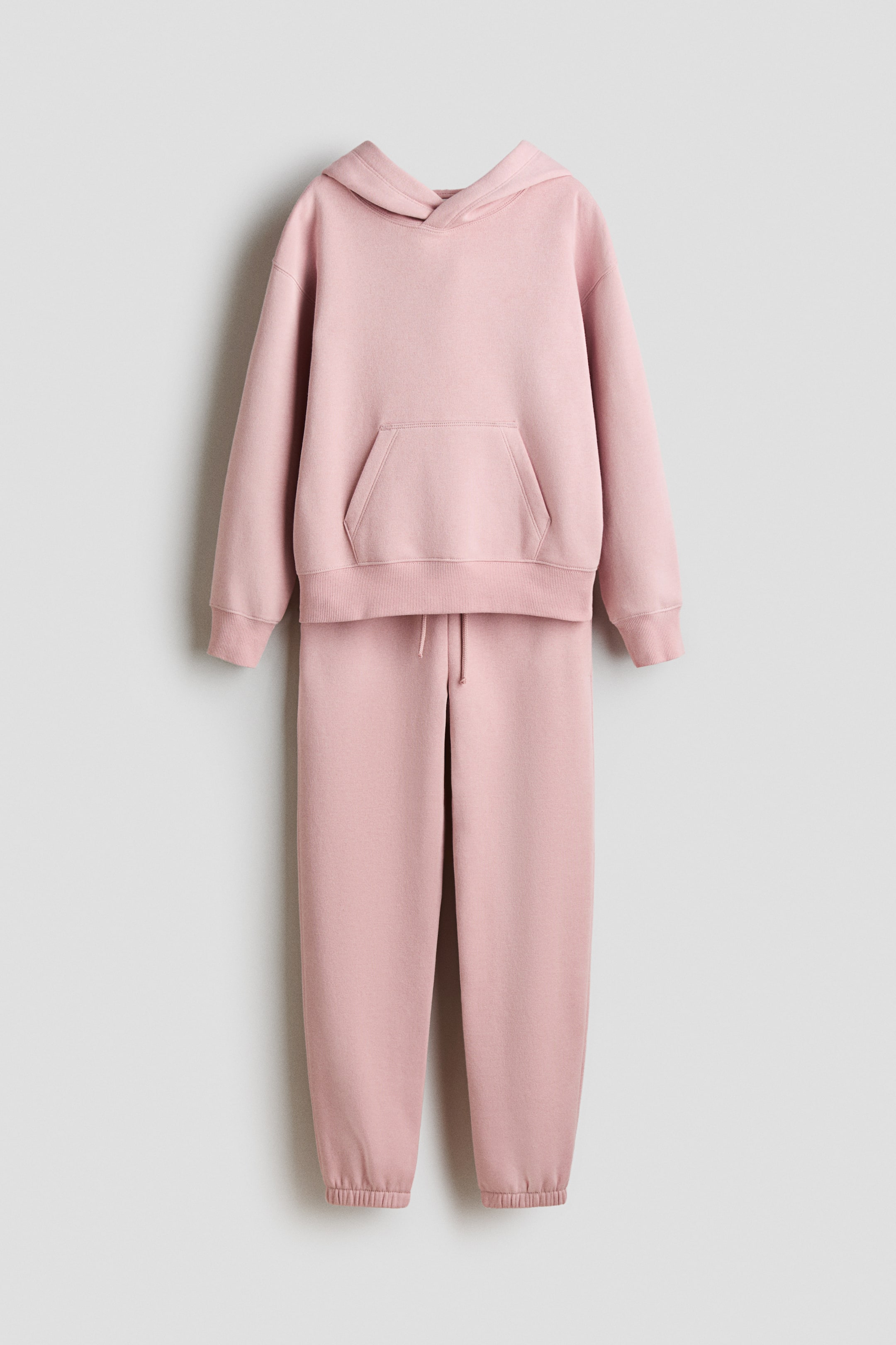 View larger image: A pink tracksuit is facing front, comprising a hoodie with a hood, a large kangaroo pocket, and ribbed cuffs and hem, and matching sweatpants displaying a drawstring waist and ribbed ankle cuffs.