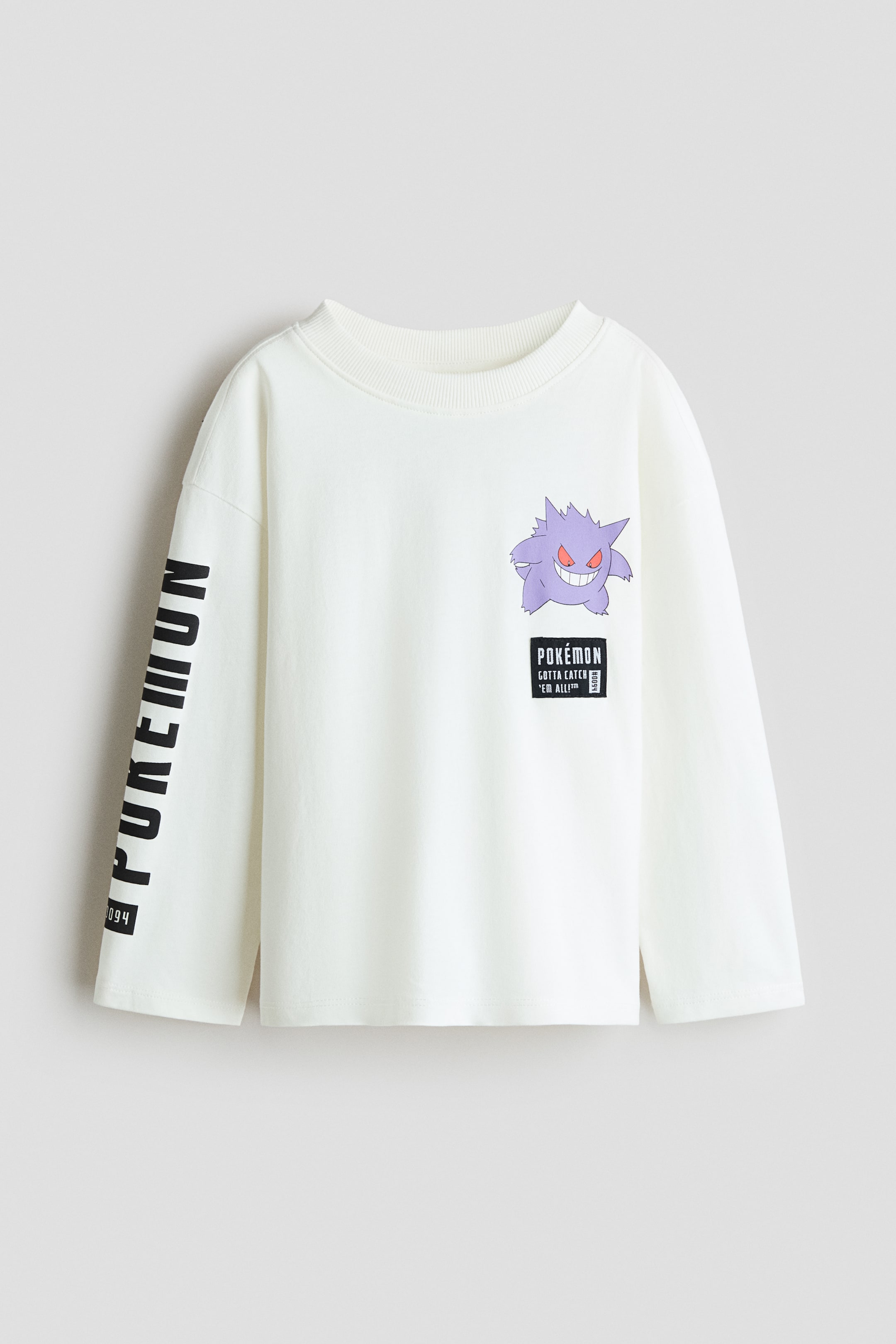 View larger image: The off-white long-sleeved top features a ribbed crew neck. A purple Gengar graphic appears on the front, positioned above a black rectangular patch with "Pokemon Gotta Catch Em All" text, while the left sleeve displays vertical "Pokemon" text with "094".