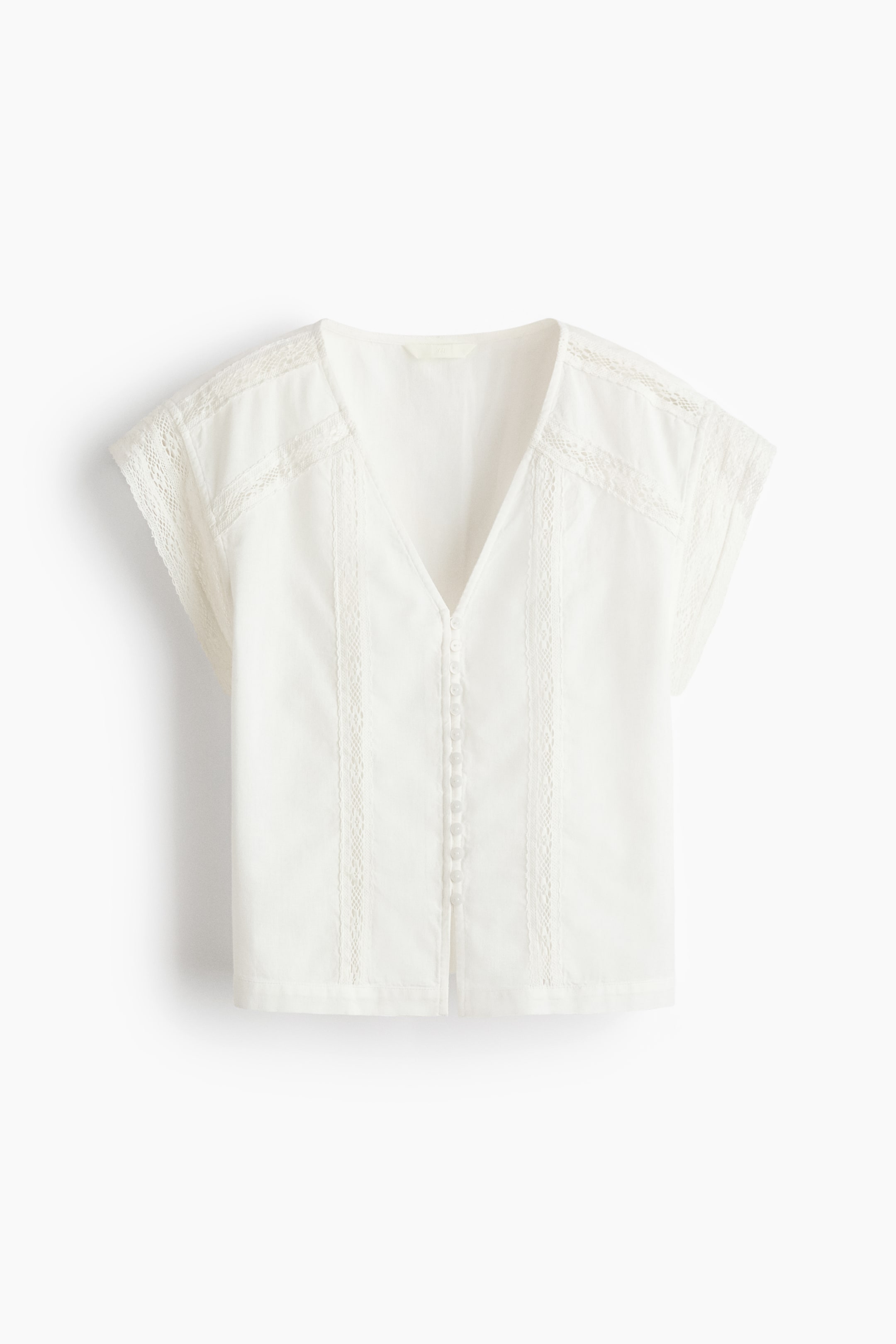 Grotere afbeelding bekijken: Een witte top wordt van voren getoond, met een V-hals en korte kapmouwtjes. Een rij kleine witte knoopjes loopt langs het midden van de voorkant, geflankeerd door verticale kanten afwerking en pintuck details, met meer kanten afwerking op de schouders.