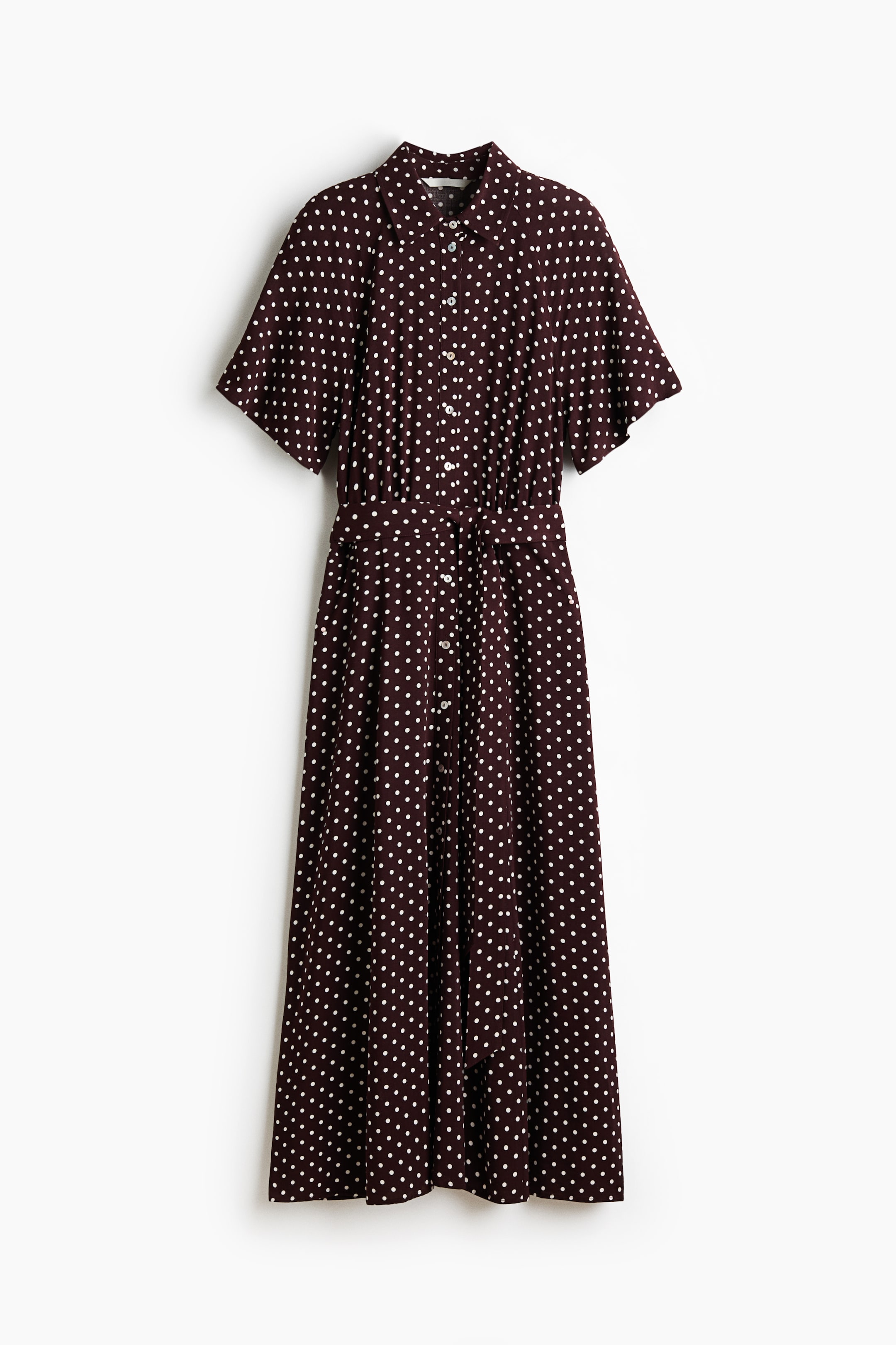 View larger image: The calf-length dress, shown from the FRONT, is crafted from dark woven fabric adorned with white polka dots. It features a collar, button-down front, short raglan sleeves, a gathered waist, and a tie belt.