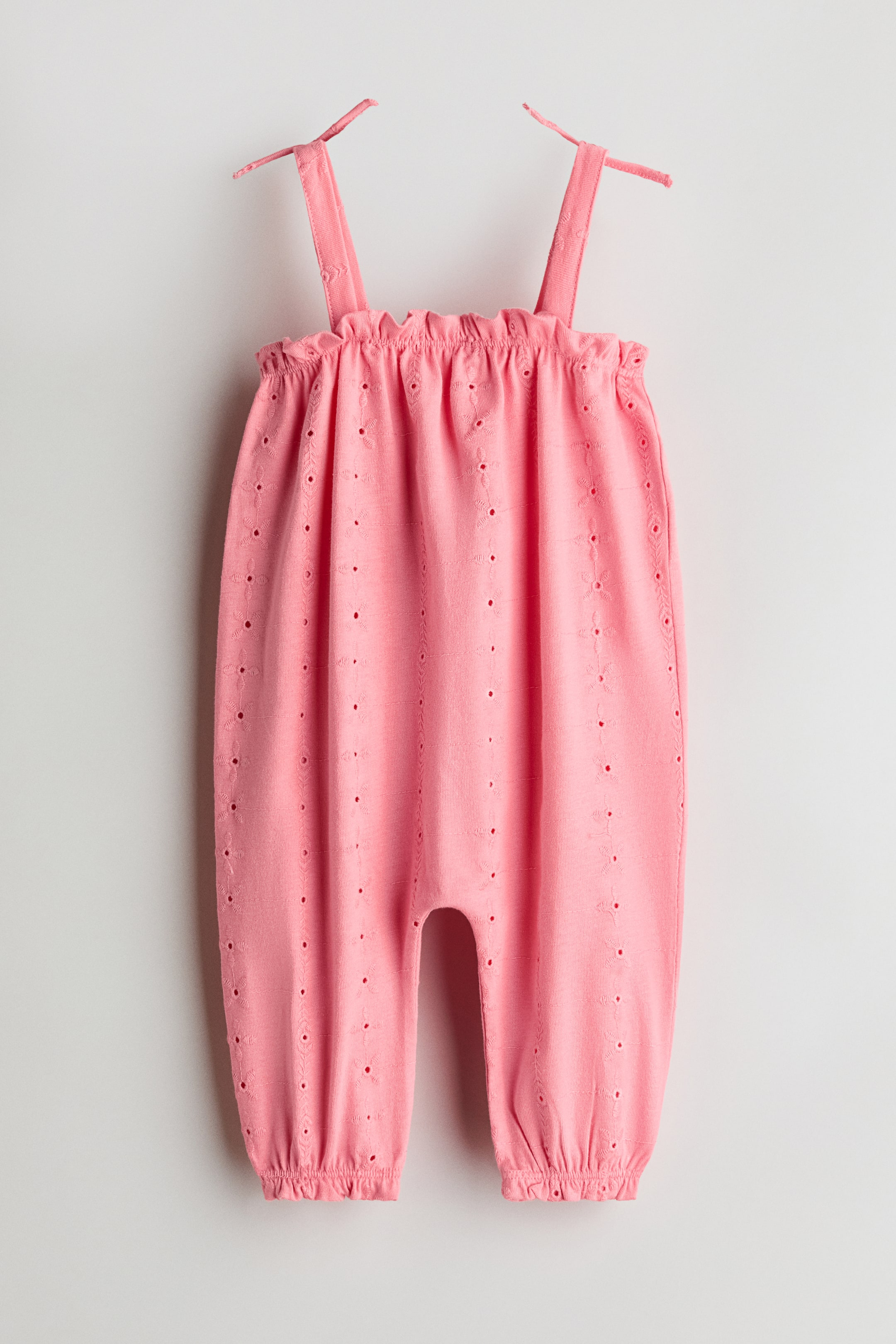 View larger image: A pink baby romper is showcasing its front, featuring all-over eyelet embroidery. It is designed with a gathered elasticized neckline, adjustable tie-straps, and elasticized ankle cuffs.