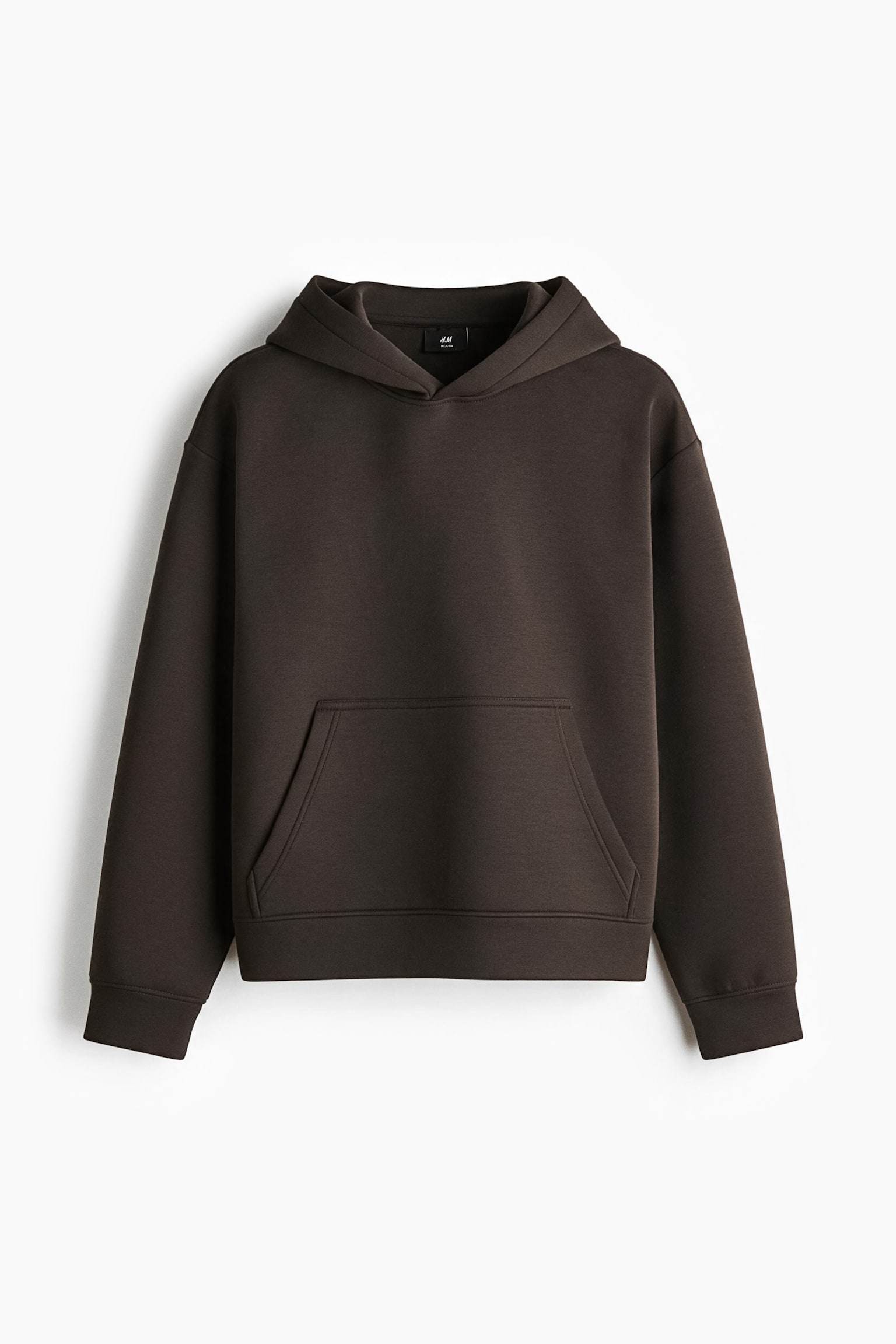 A dark brown hoodie in structured scuba fabric is shown from the front, featuring a loose fit with dropped shoulders and long sleeves. The design includes a double-layered hood, a front kangaroo pocket, and wide trim at the cuffs and hem.