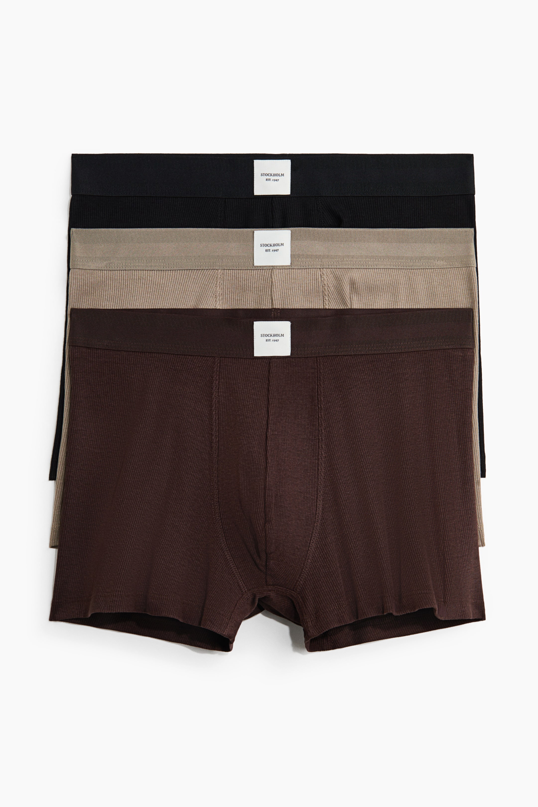 View larger image: Three pairs of boxer briefs are stacked, presenting their FRONT view; the top pair is black, the middle is beige, and the bottom is dark brown. Each pair features a ribbed knit texture and an elastic waistband with a white "STOCKHOLM EST. 1947" label.