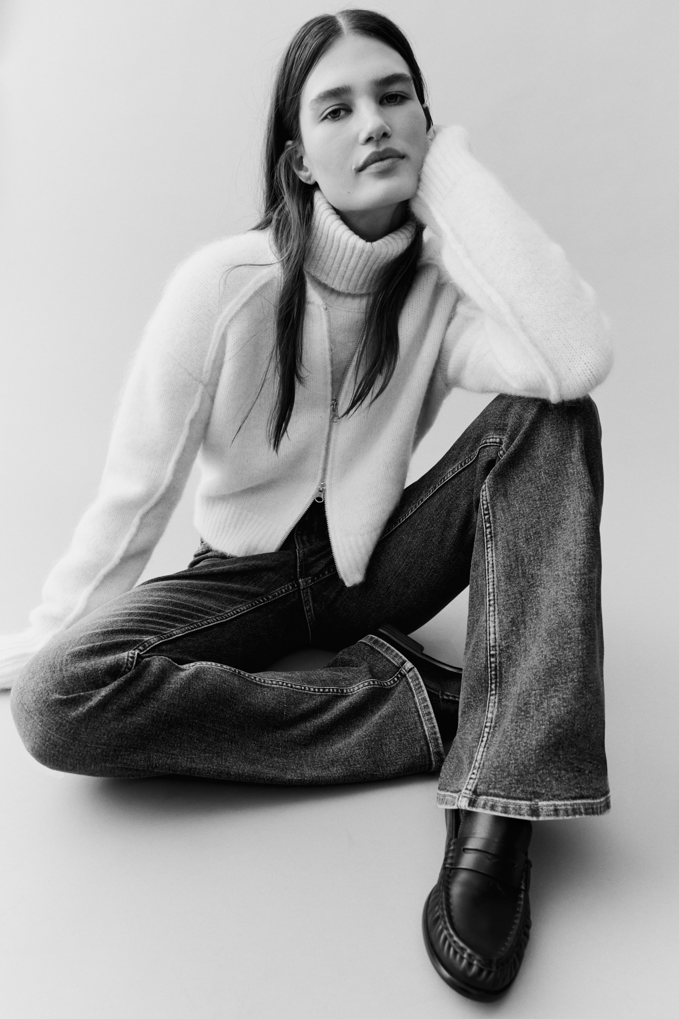 View larger image: The model is wearing dark-wash denim jeans, featuring a high waist and a visible zip fly with button closure. The jeans have wide, flared hems and front pockets with decorative stitching.