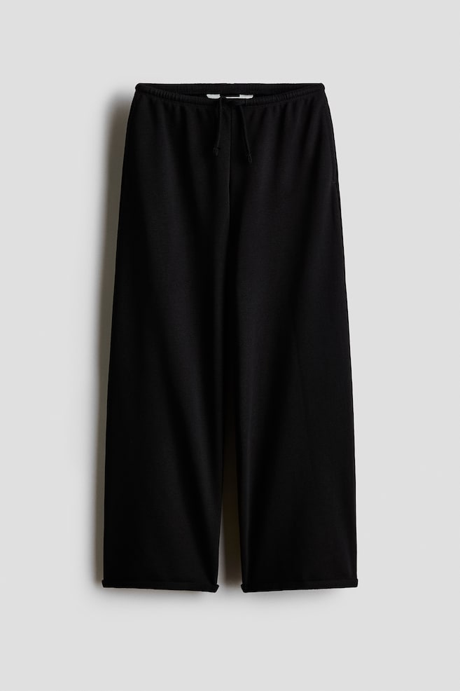 Black joggers feature a lightweight sweatshirt fabric, an elasticated drawstring waist and discreet side-seam pockets. The front view shows wide legs finishing with rolled edges at the hems. - 1
