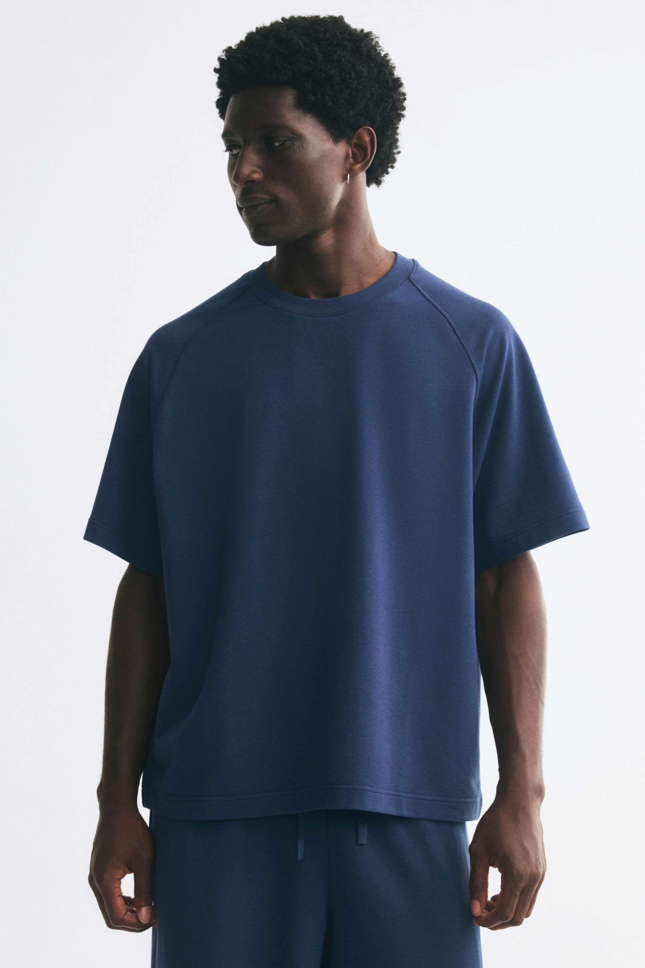 Voir une image plus grande: Le mannequin porte un t-shirt en jersey épais bleu foncé, de coupe décontractée, doté d’un col rond avec bord-côte et de manches raglan courtes. Le t-shirt est agencé avec un bas assorti à cordon de serrage.