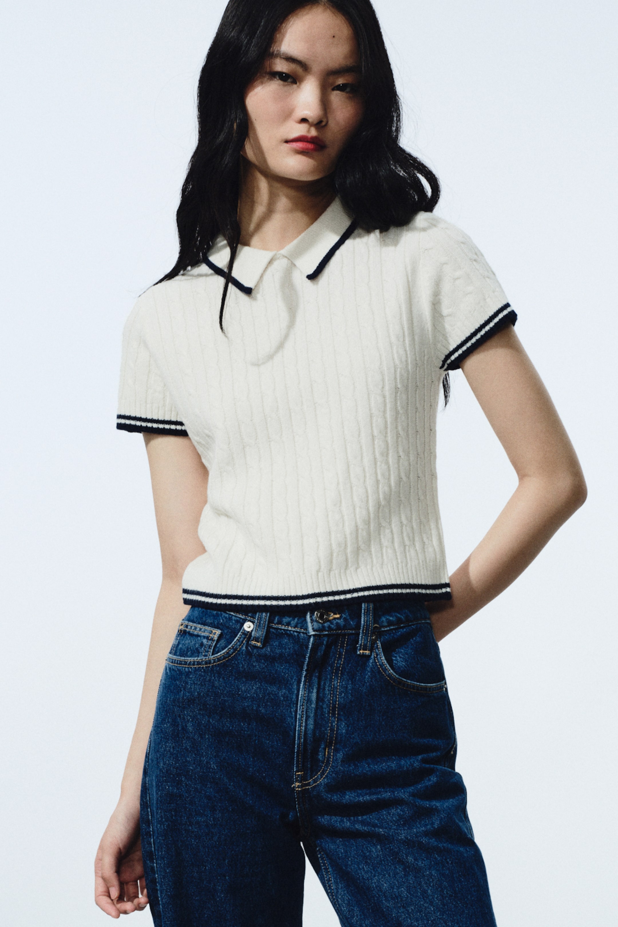 이미지 확대 보기: 크림 컬러의 케이블 니트 폴로 셔츠로, 폴로 칼라와 짧은 소매, 크롭 기장의 밑단을 갖춘 디자인이며 다크 네이비 트림으로 마감되어 있습니다.