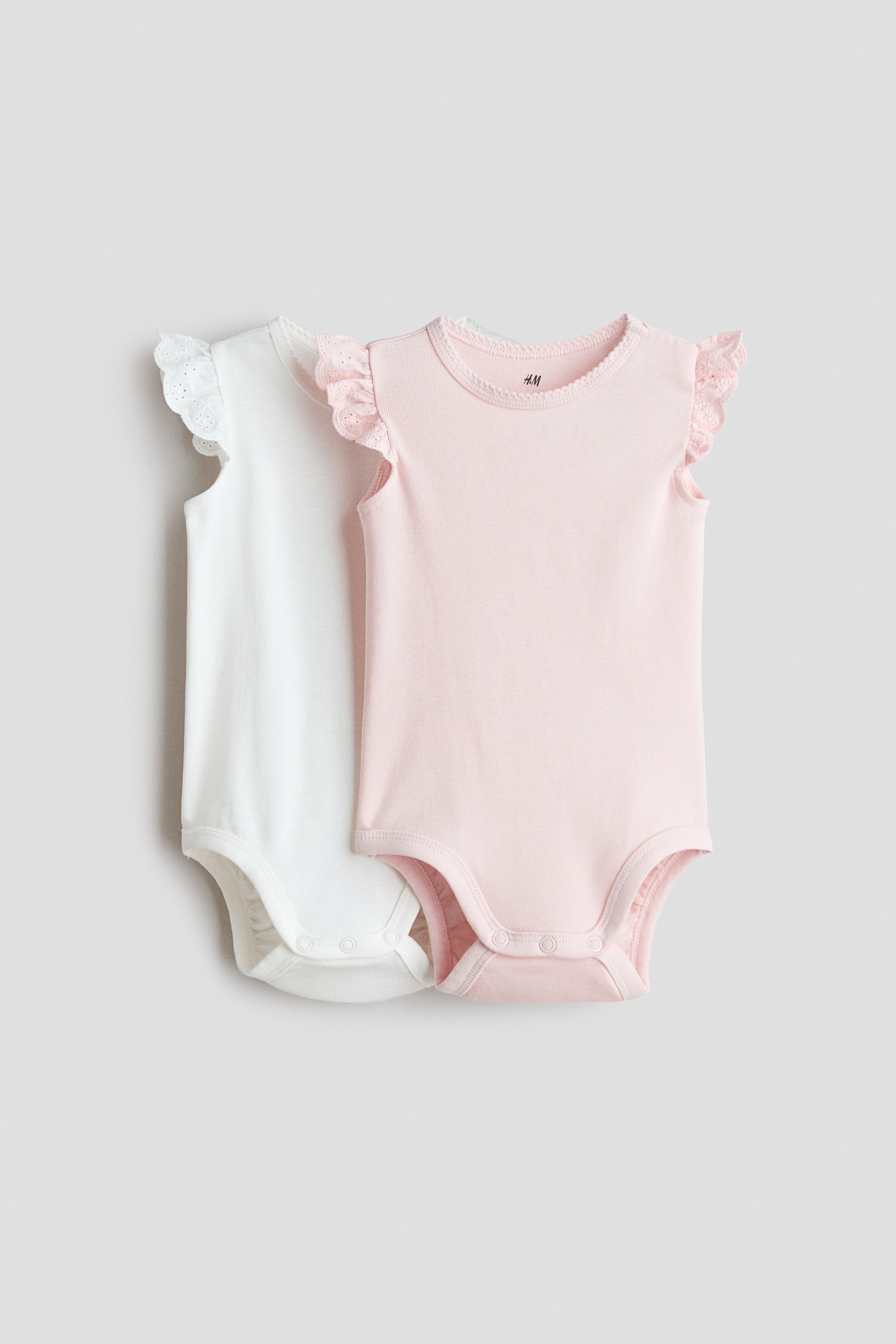 View larger image: The two baby bodysuits feature short ruffled sleeves adorned with eyelet lace detailing, a round neckline enhanced by picot trim, and convenient snap closures at the crotch. Showcasing a front-facing design, the bodysuits come in two charming colors: classic white and soft light pink.