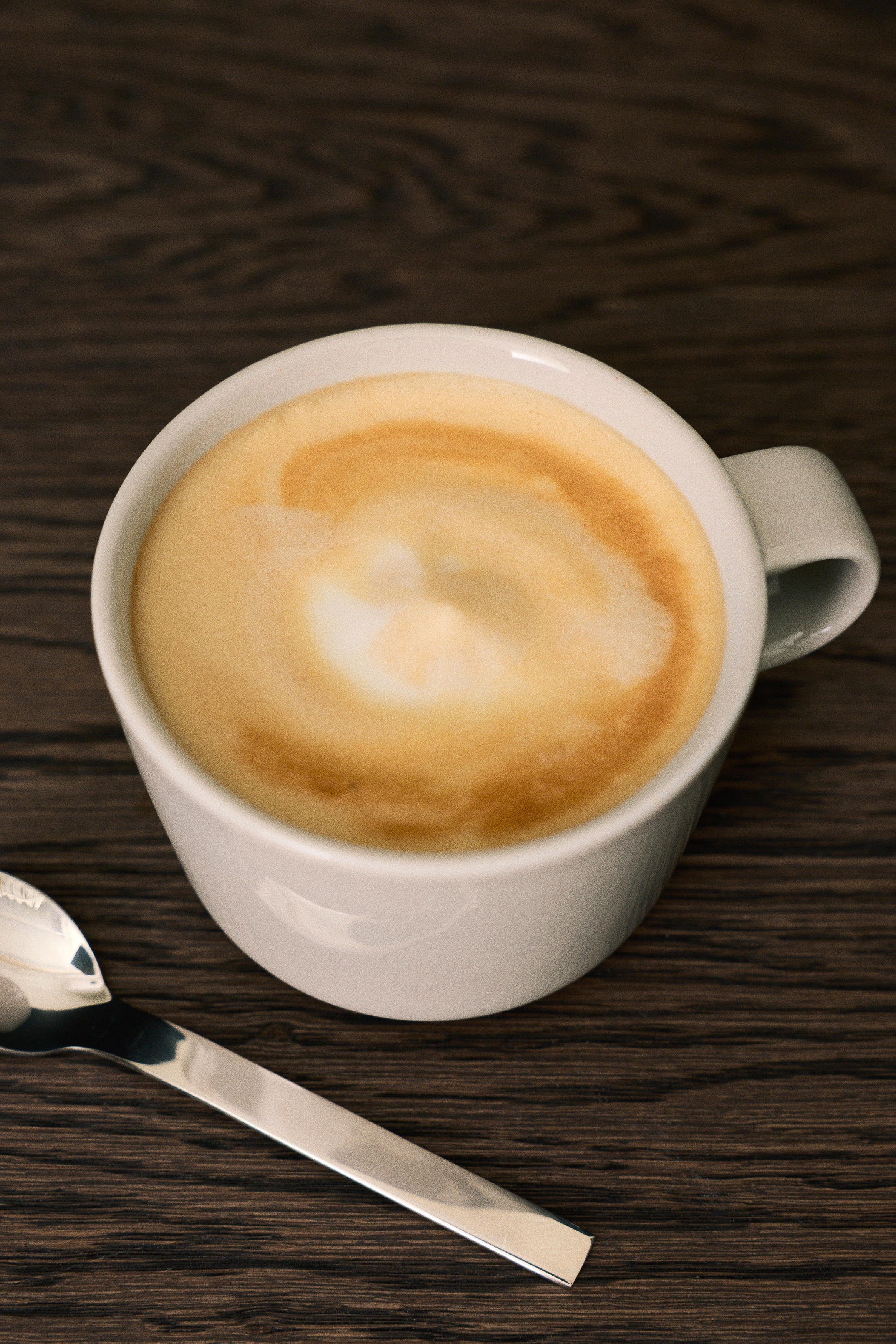 Dos tazas de color beige claro están colocadas una al lado de la otra, cada una con un cuerpo cilíndrico sutilmente cónico, una base redondeada y un asa en forma de C.