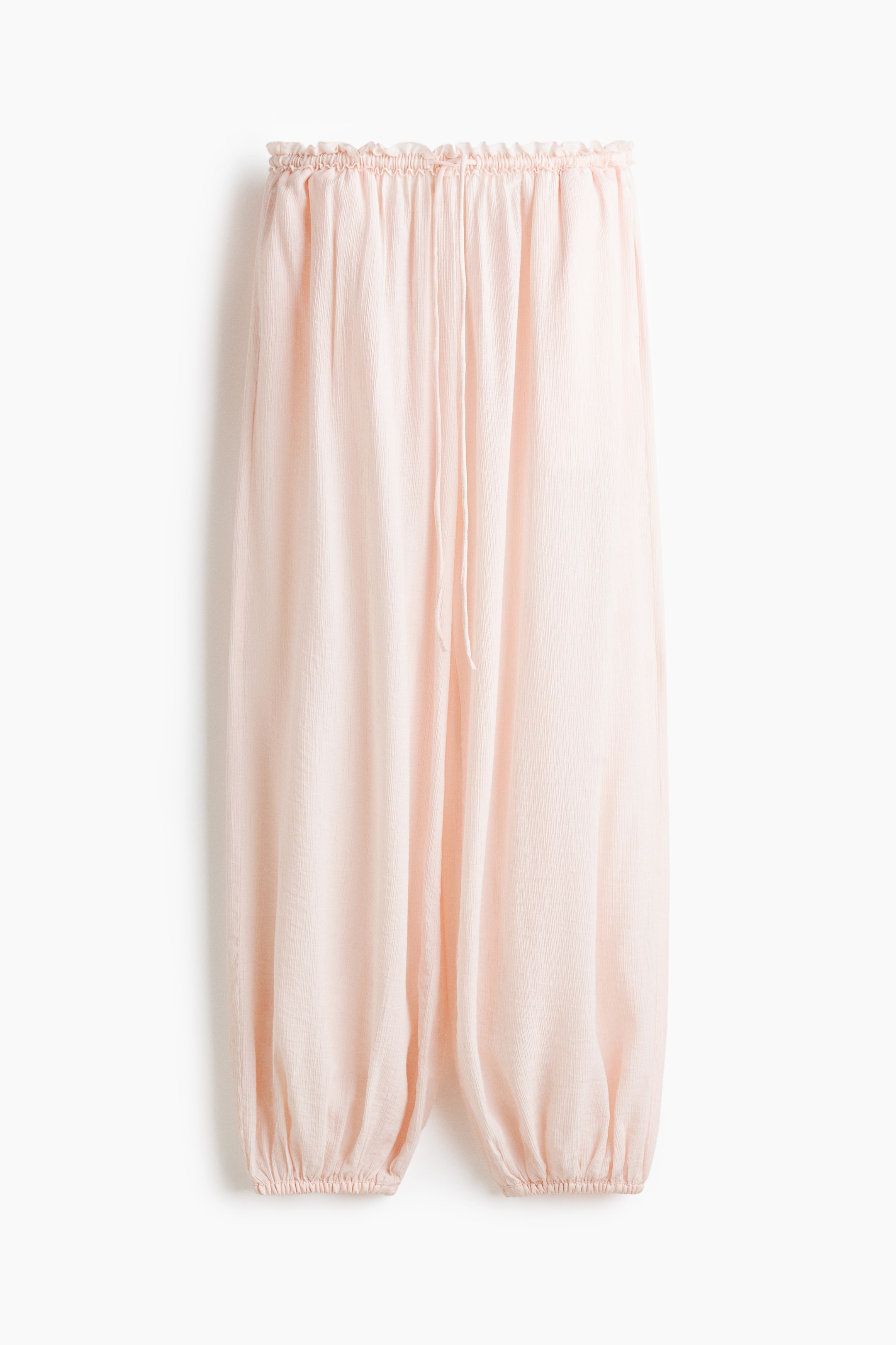 View larger image: Balloon drawstring trousers are showcased in a light pink, crinkled fabric, viewed from the front. They feature an elasticated, ruched waistband with a visible drawstring and gather at the elasticated cuffs, forming a voluminous balloon silhouette.