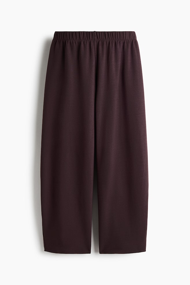These dark brown wide-leg trousers are shown from the front, featuring a gathered elasticated waistband and a relaxed, draped silhouette. The trousers have wide, straight legs with a clean, unadorned hem. - 1