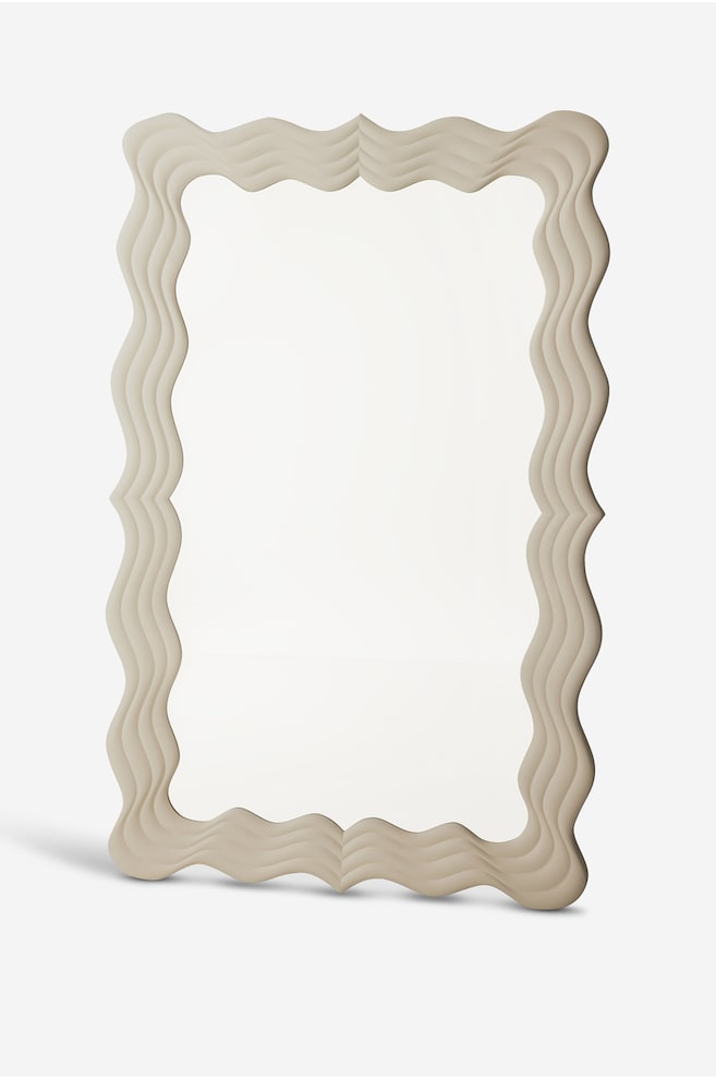 Een rechthoekige spiegel staat in een lichte hoek en heeft een dik frame in een matte beige afwerking met een gelaagd, golvend ontwerp. De vormgegeven randen creÃ«ren een geribbelde textuur rondom het heldere, reflecterende glas. - 1