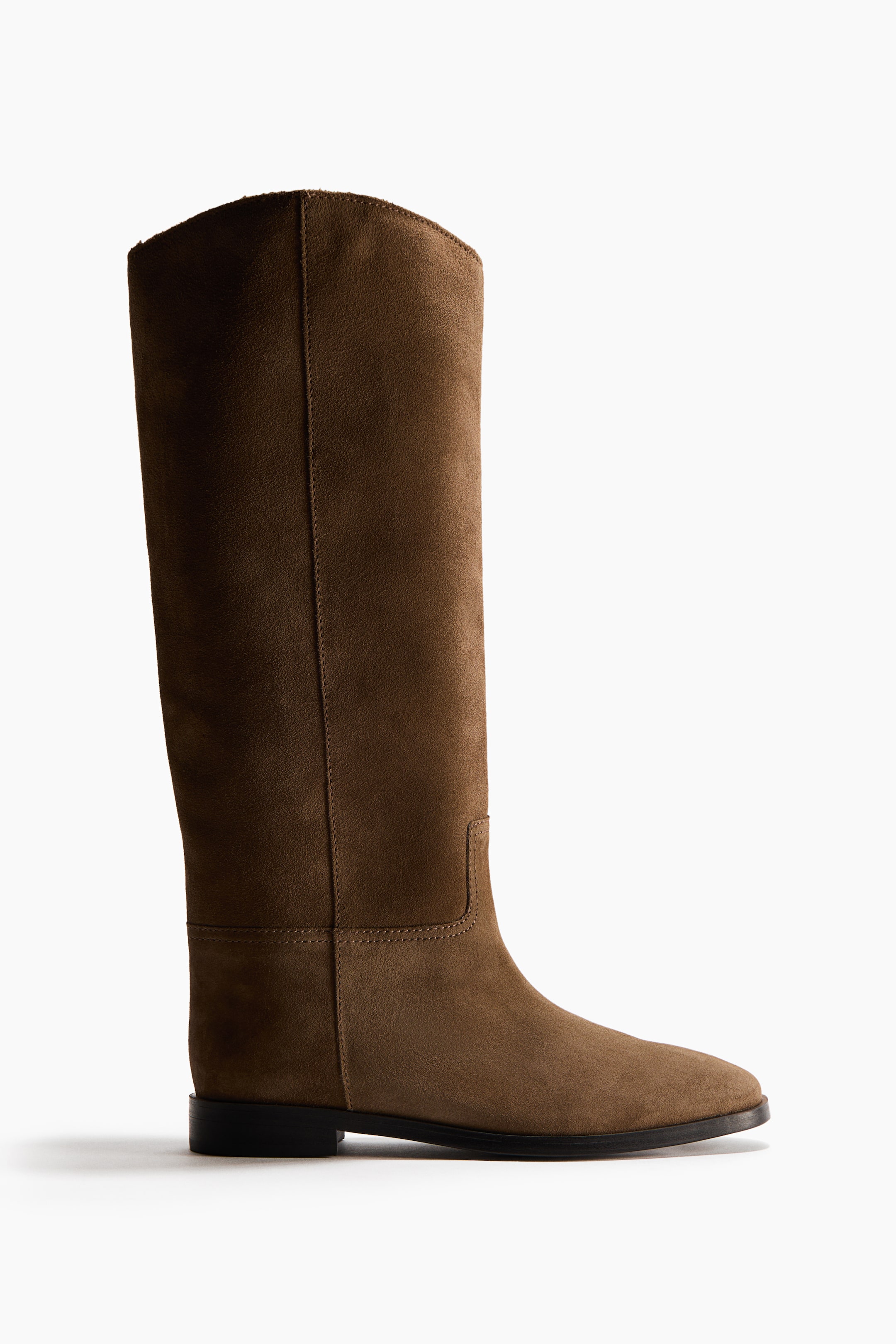 Größeres Bild ansehen: Ein brauner hoher Stiefel aus Wildleder zeigt nach rechts, mit einer abgerundeten Spitze und einem niedrigen Blockabsatz. Der Schaft präsentiert sichtbare vertikale und horizontale Nahtdetails sowie eine leicht geschwungene obere Kante.