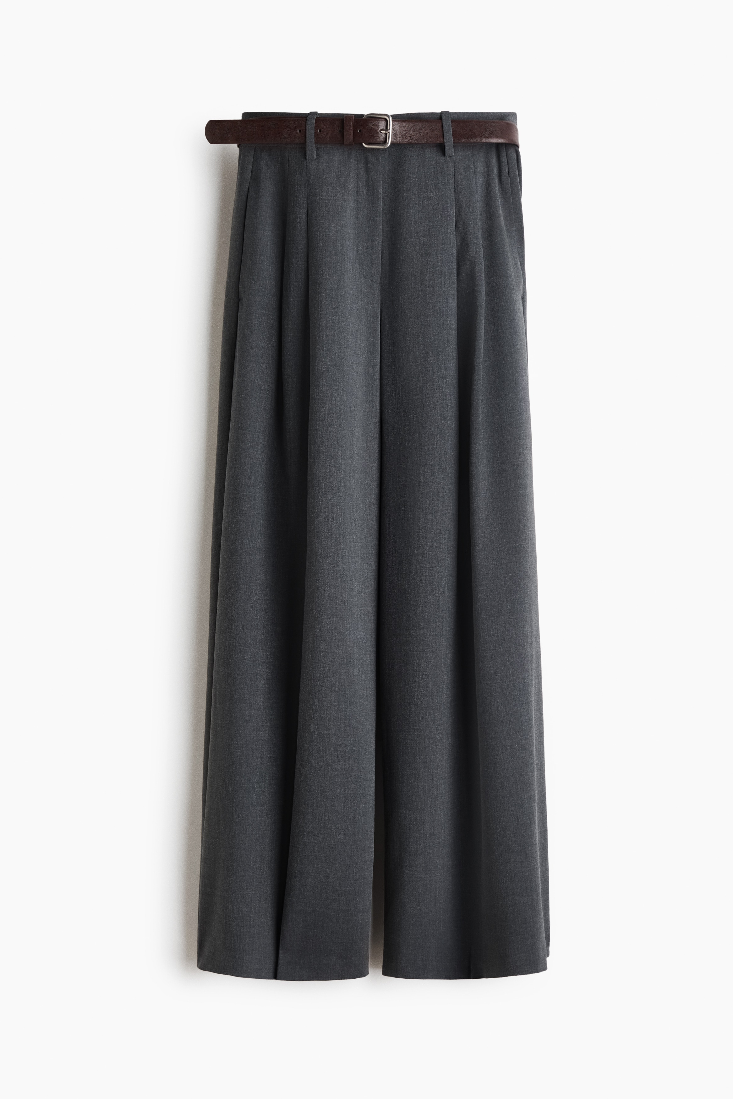 La modelo lleva pantalones de corte holgado en tela tejida gris oscuro, con cintura alta y pinzas delanteras, lÃ­neas marcadas y piernas anchas. Los pantalones se combinan con un cinturÃ³n ajustable cafÃ© oscuro con hebilla de metal y un suÃ©ter gris en capas, metido por dentro.