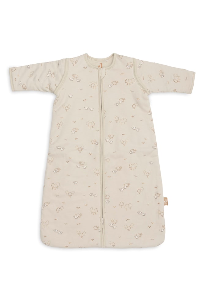 Une gigoteuse pour bébé beige clair à manches longues est présentée à plat, vue de face, mettant en valeur un motif intégral composé de petits moutons, arbres et oiseaux dessinés en contour. Elle présente un col arrondi et une fermeture éclair centrale sur toute la longueur, descendant jusquâau bas arrondi et fermé. - 1
