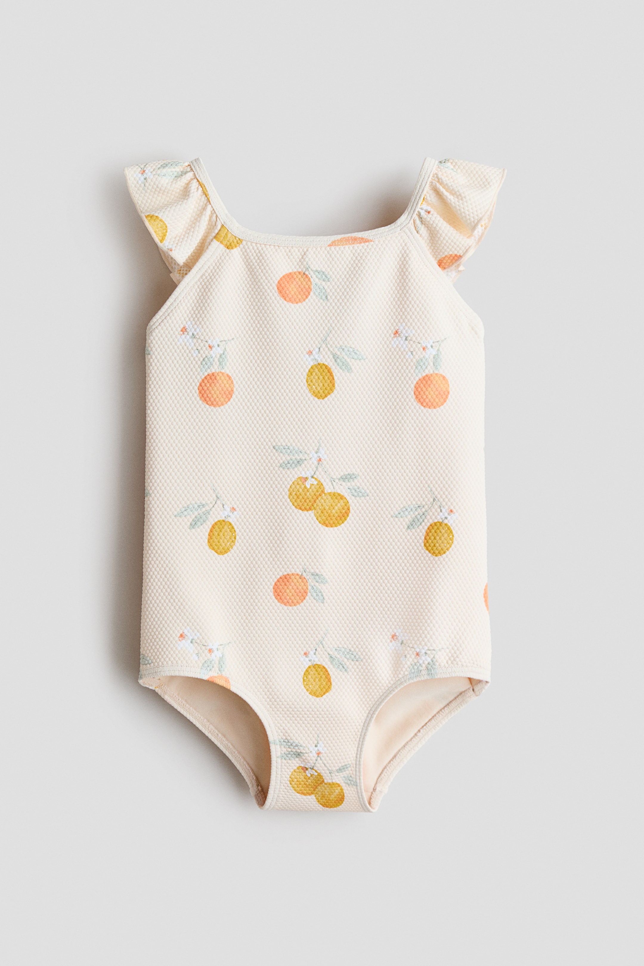 Größeres Bild ansehen: Der H&M Adorables Badeanzug wird von vorne präsentiert, hergestellt aus einem strukturierten Stoff und mit Zitrusfrüchten gemustert. Er verfügt über einen quadratischen Ausschnitt und Rüschen-Träger mit versäuberten Kanten.
