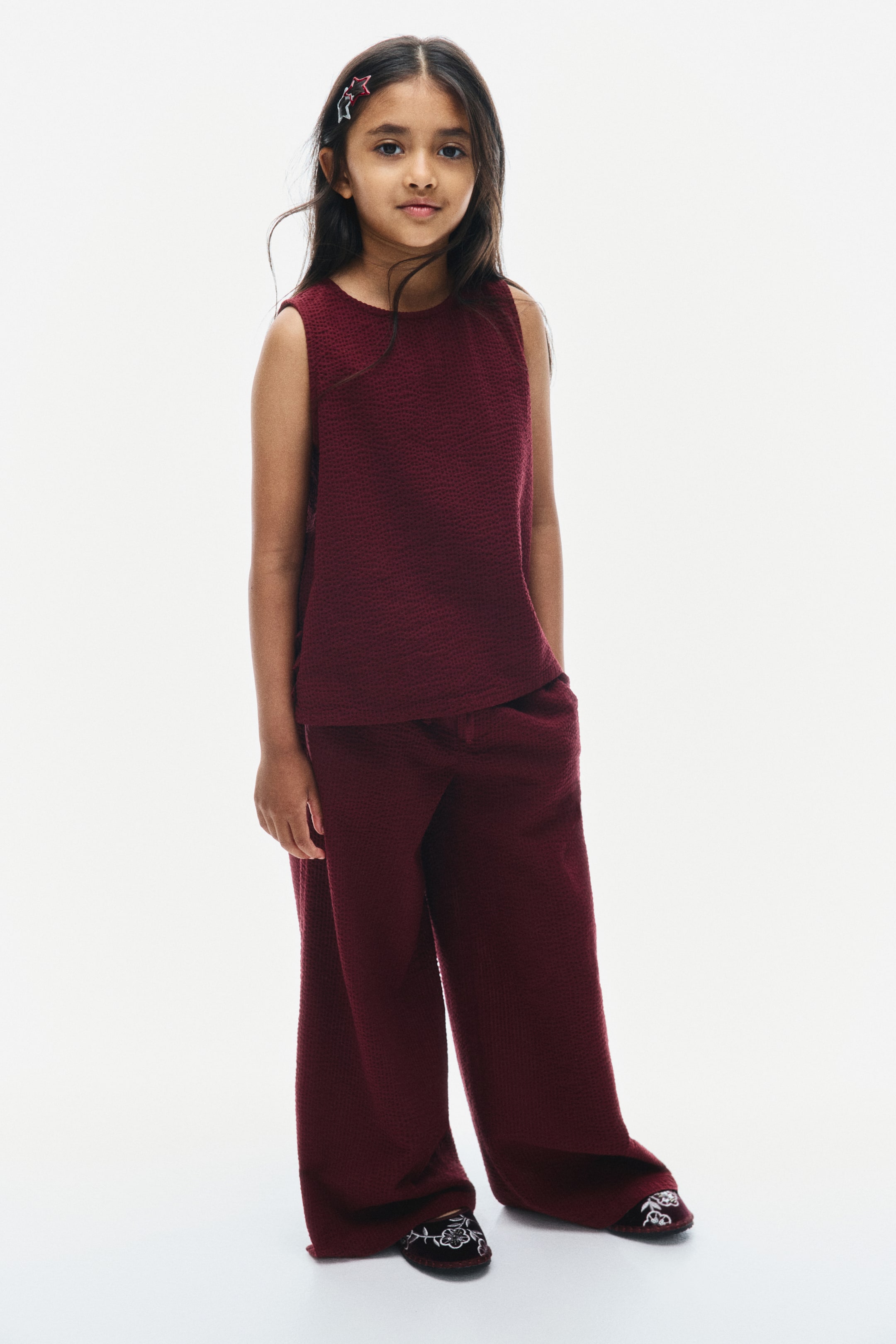 View larger image: A dark red cotton seersucker set is shown from the front, featuring a sleeveless top with a round neckline and matching straight-leg pants. The top hangs loosely at the hips, while the pants drape down to the feet in a relaxed fit.