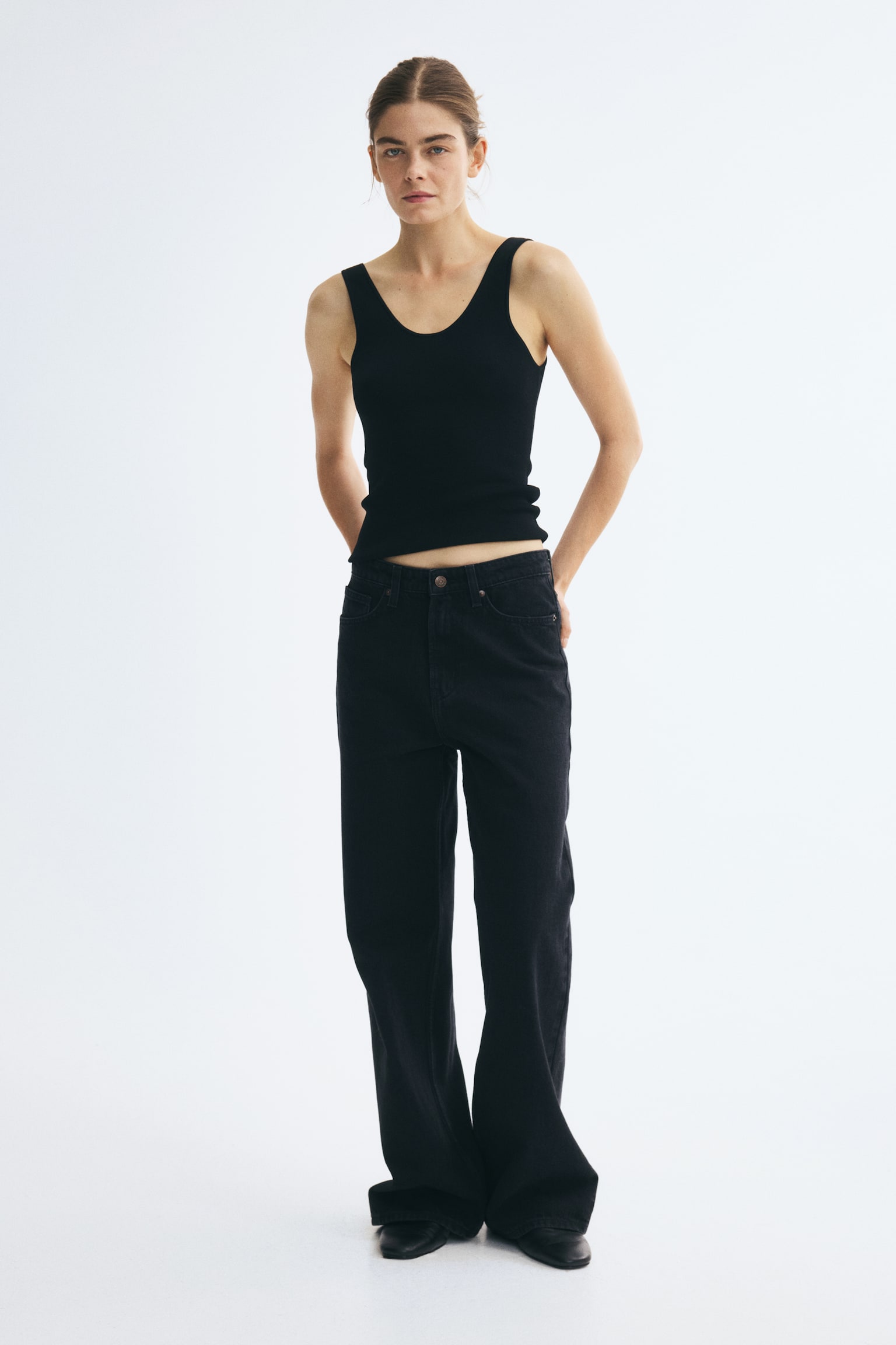 A pair of washed black wide-leg jeans is hanging front-facing, featuring a classic five-pocket design with metallic rivets and belt loops. The jeans show a high-rise waist and a loose, straight-cut wide-leg silhouette. - 1