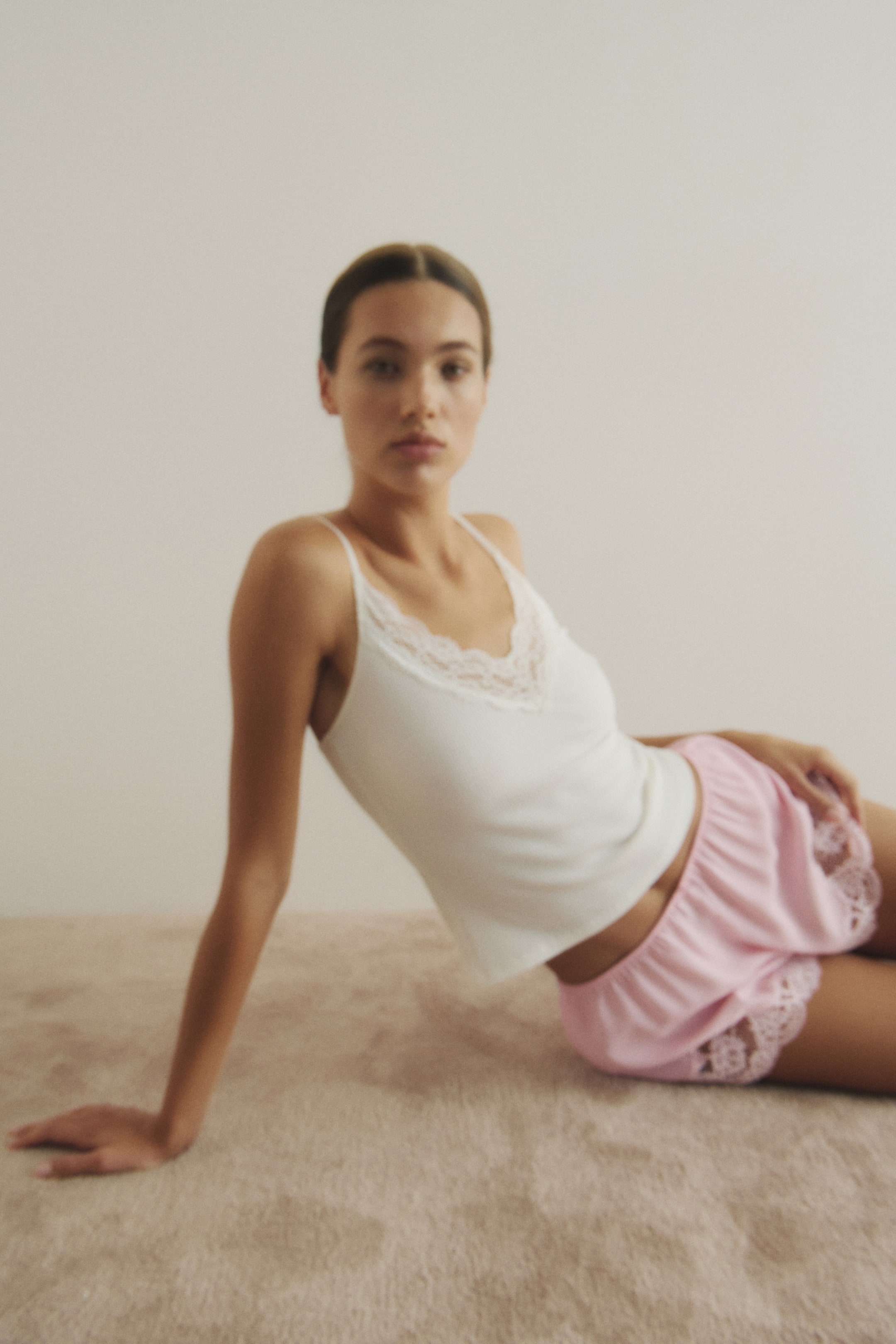 Visualizza immagine più grande: Viene presentato un completo composto da una canotta bianca e pantaloncini rosa. La canotta bianca è caratterizzata da spalline sottili e da una scollatura a V rifinita con pizzo bianco. I pantaloncini rosa hanno la vita elasticizzata e un bordo in pizzo rosa coordinato lungo l'orlo delle gambe.