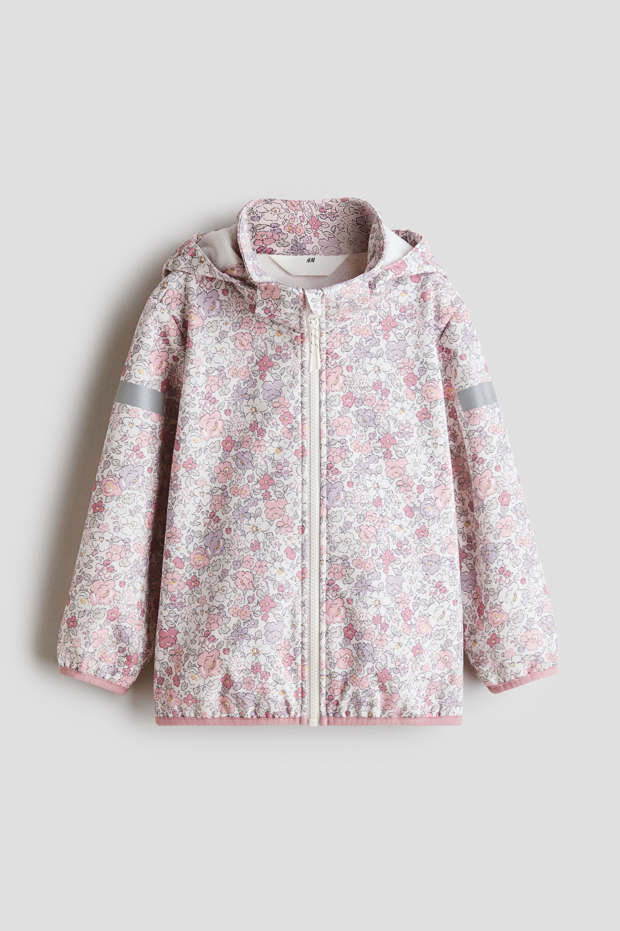 View larger image: The jacket with a hood is showcased front-facing, highlighting a white base adorned with a subtle floral pattern in shades of pink and purple. It comes with a full-length white zipper down the center, elasticized pink cuffs and hem, and reflective strips on each sleeve.
