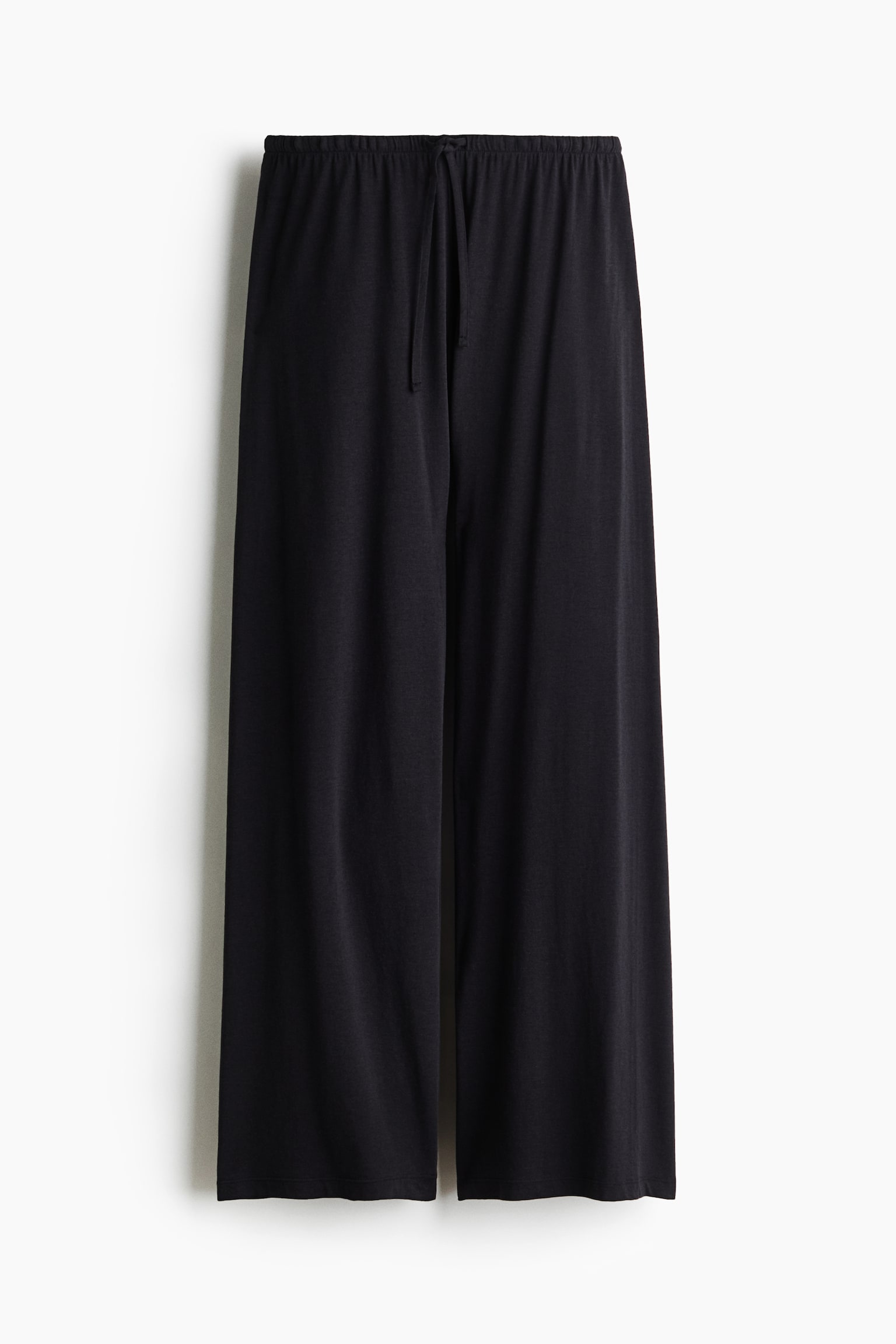 Black loose-fit pyjama pants are hanging straight, featuring an elasticated waistband with a matching drawstring tied at the centre and wide, relaxed-fit legs. - 1