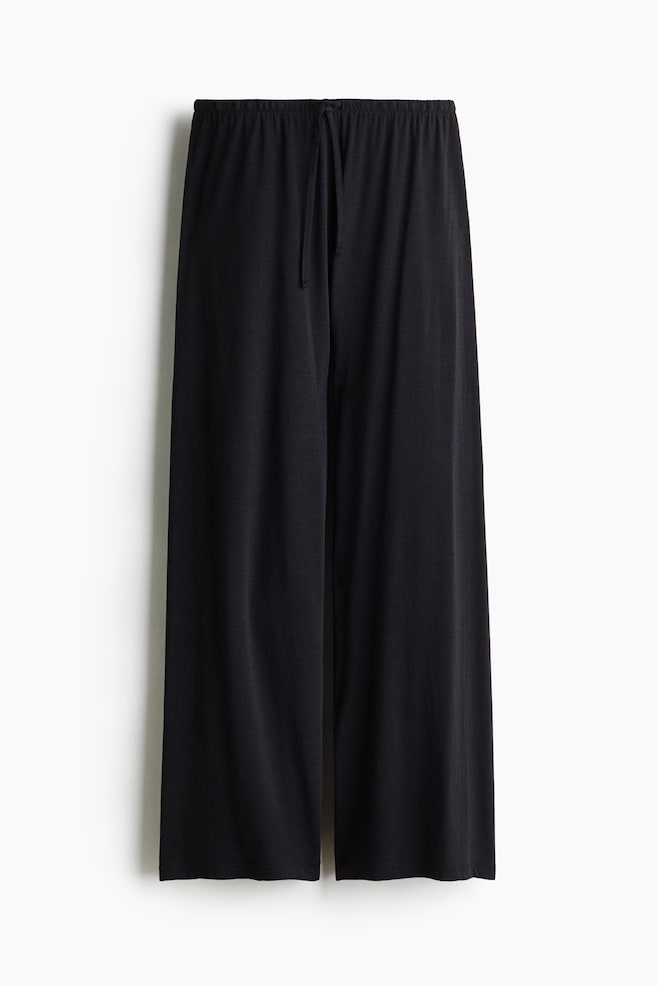 Pantaloni del pigiama neri a vestibilità morbida sono appesi diritti, con vita elasticizzata e coulisse coordinata annodata al centro, e gambe ampie dalla vestibilità rilassata. - 1