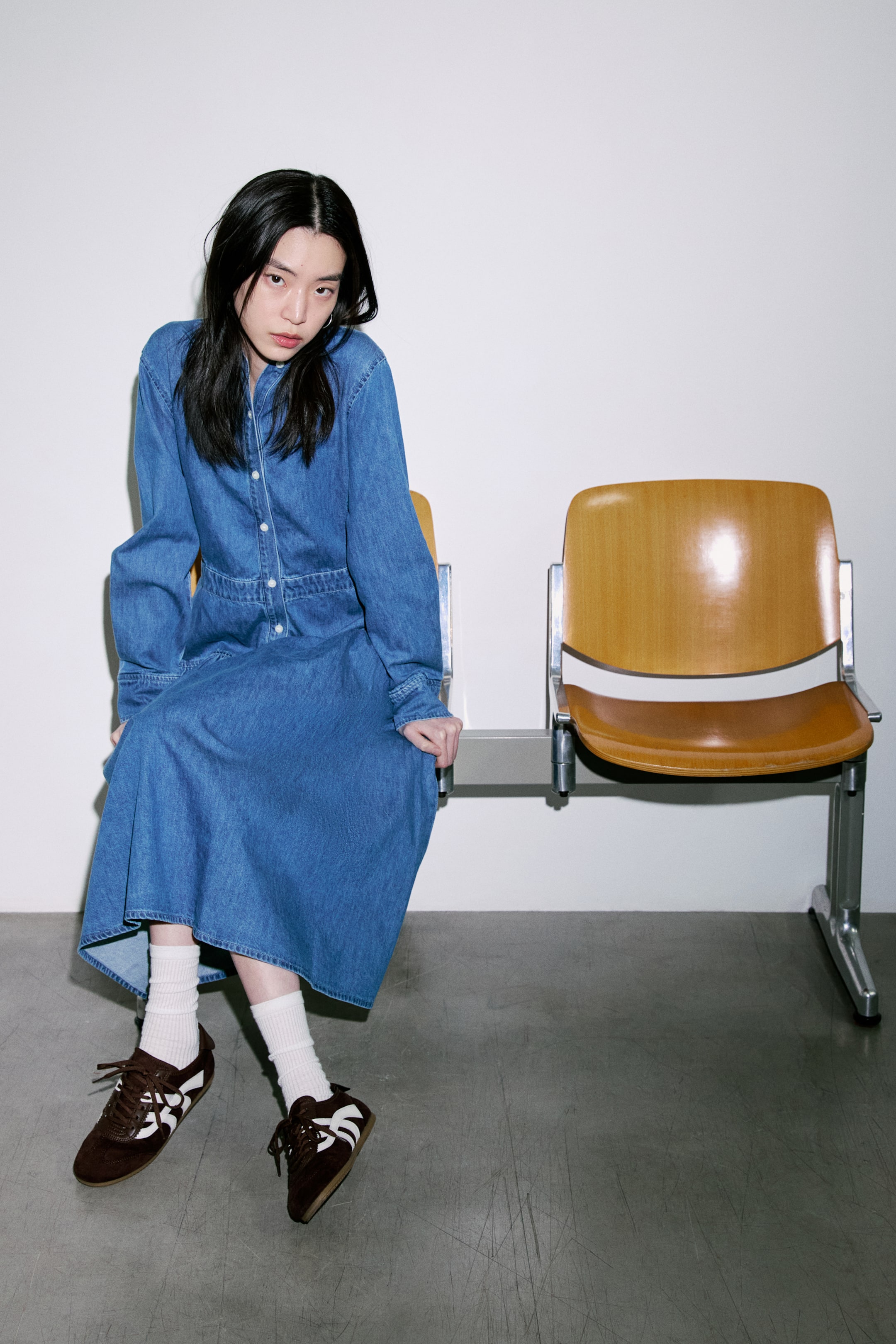 拡大画像を表示: ブルーデニムのミディドレスは、襟付きのネックライン、フロントに並ぶフルボタンのプラケット、そしてボタン付きのカフスがついた長袖が特徴です。定義されたウエストバンドが、ボタン付きのボディスとAラインのミディスカートを分けています。