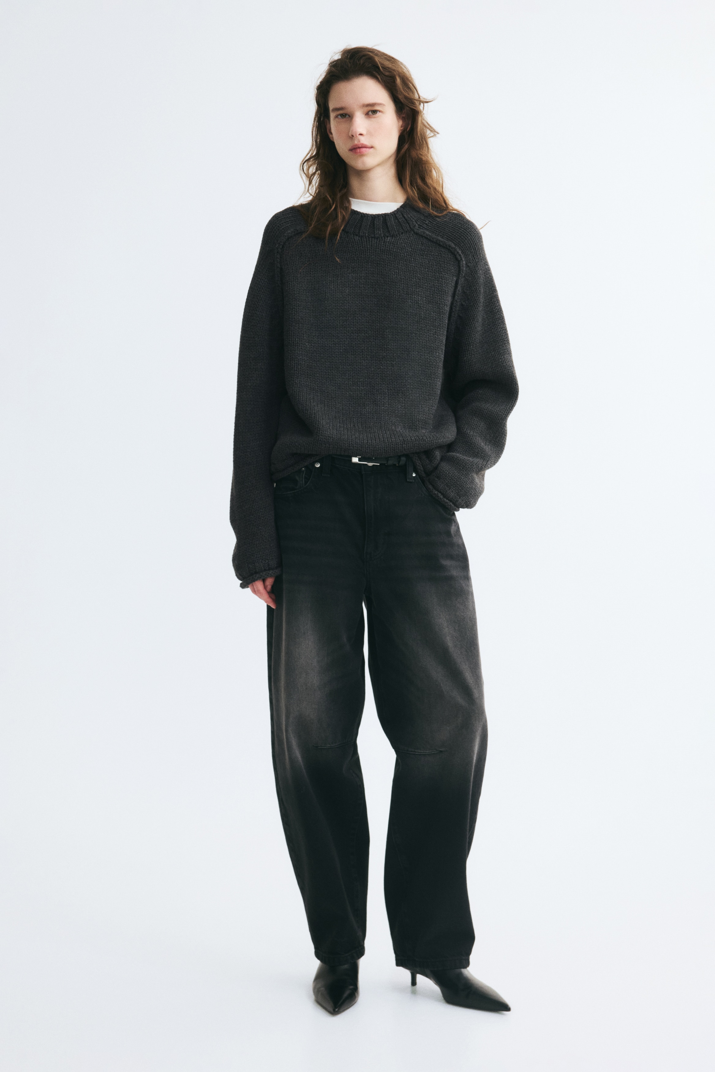 A dark grey knitted jumper is shown from the front, featuring a ribbed crew neck, raglan sleeves, and ribbed detailing at the cuffs and hem.