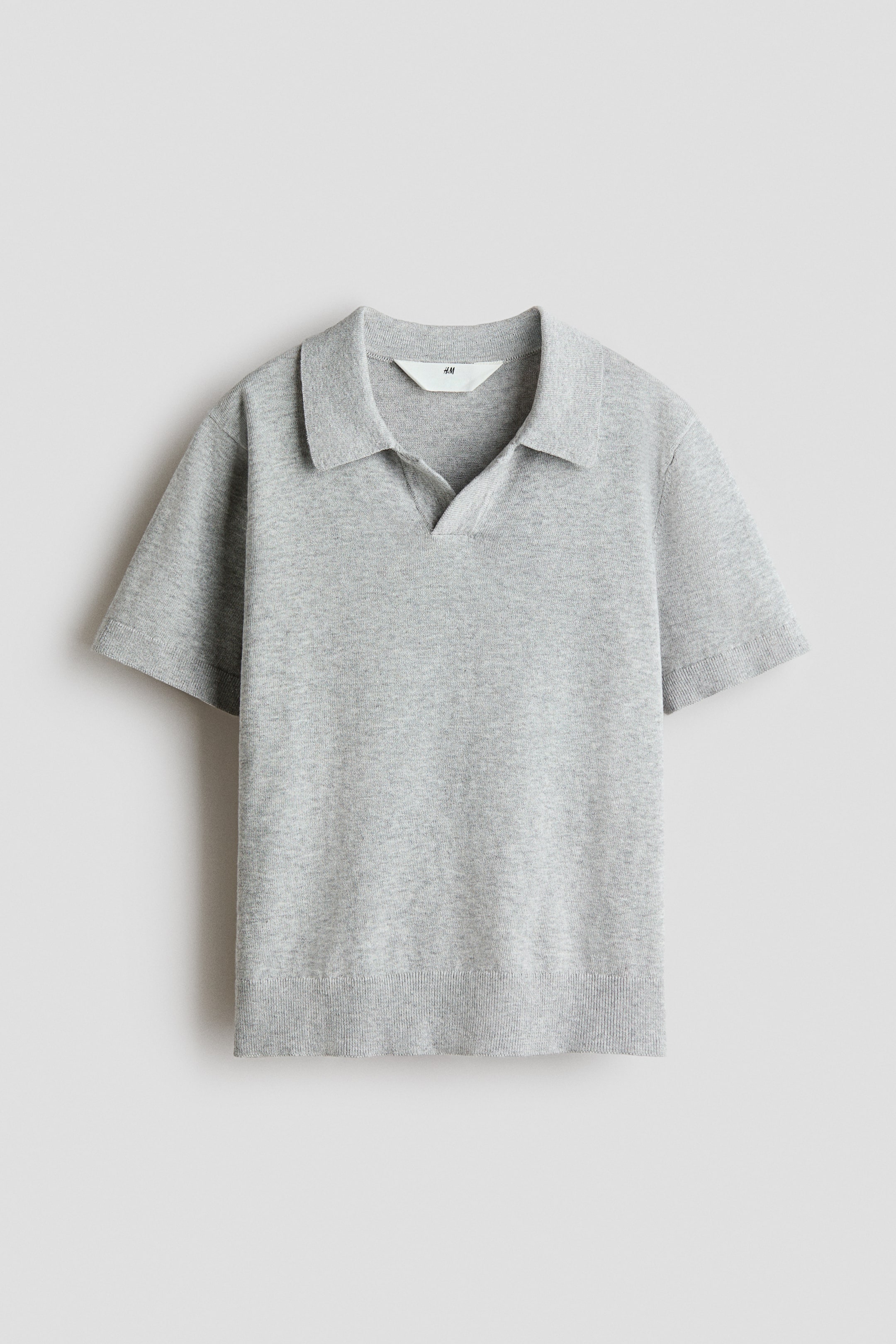 Agrandir l'image: Un polo en coton finement tricoté de couleur gris clair est présenté de face. Il est doté d'un col classique avec une ouverture en forme de V, de manches courtes, ainsi que de poignets et d'un ourlet côtelés.