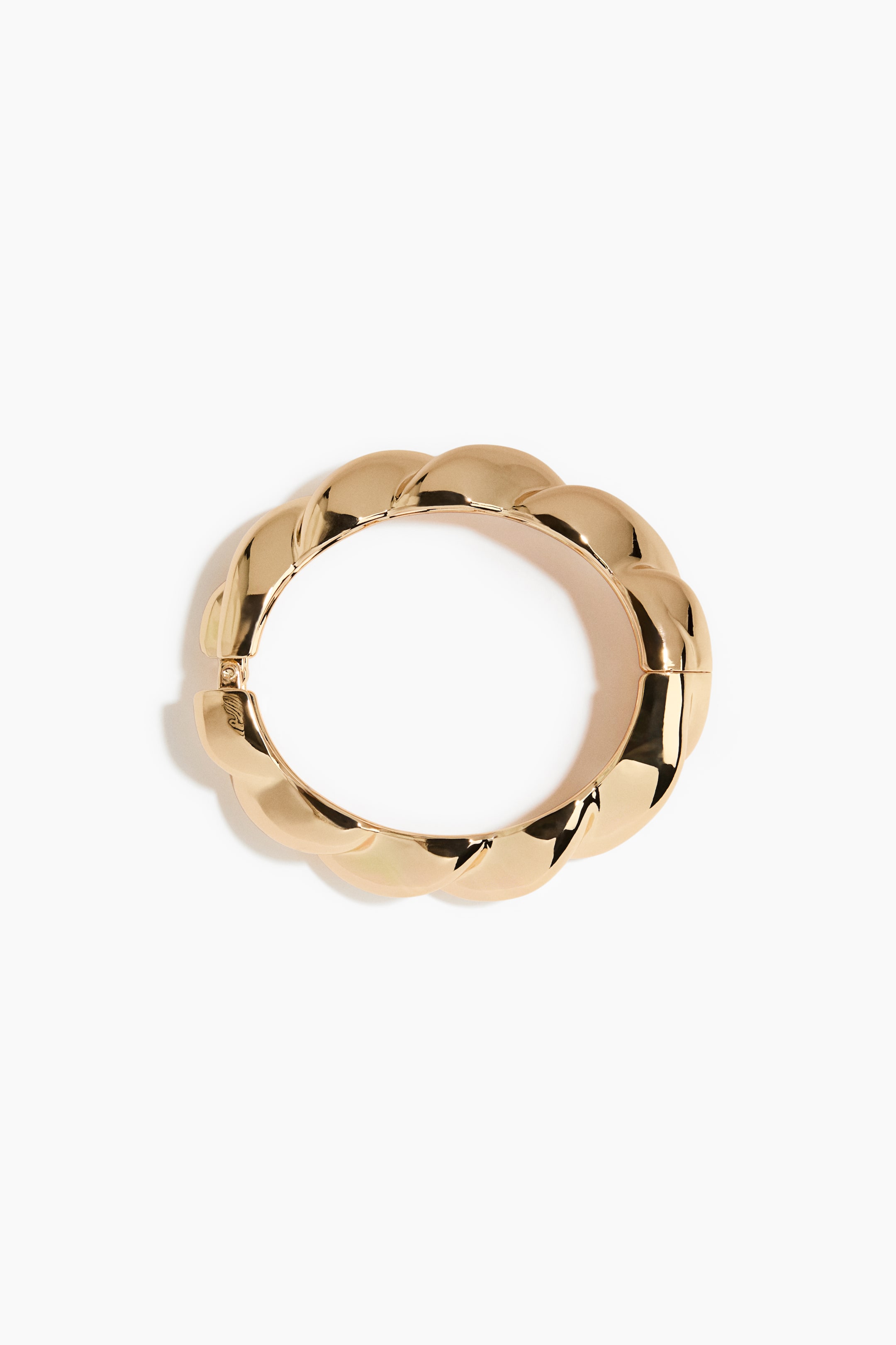 Agrandir l'image: Un bracelet jonc articulé de teinte dorée est présenté de face, avec un design imposant torsadé façon croissant et une finition hautement polie. Le bracelet circulaire repose à plat, mettant en évidence un mécanisme de charnière visible sur un côté.