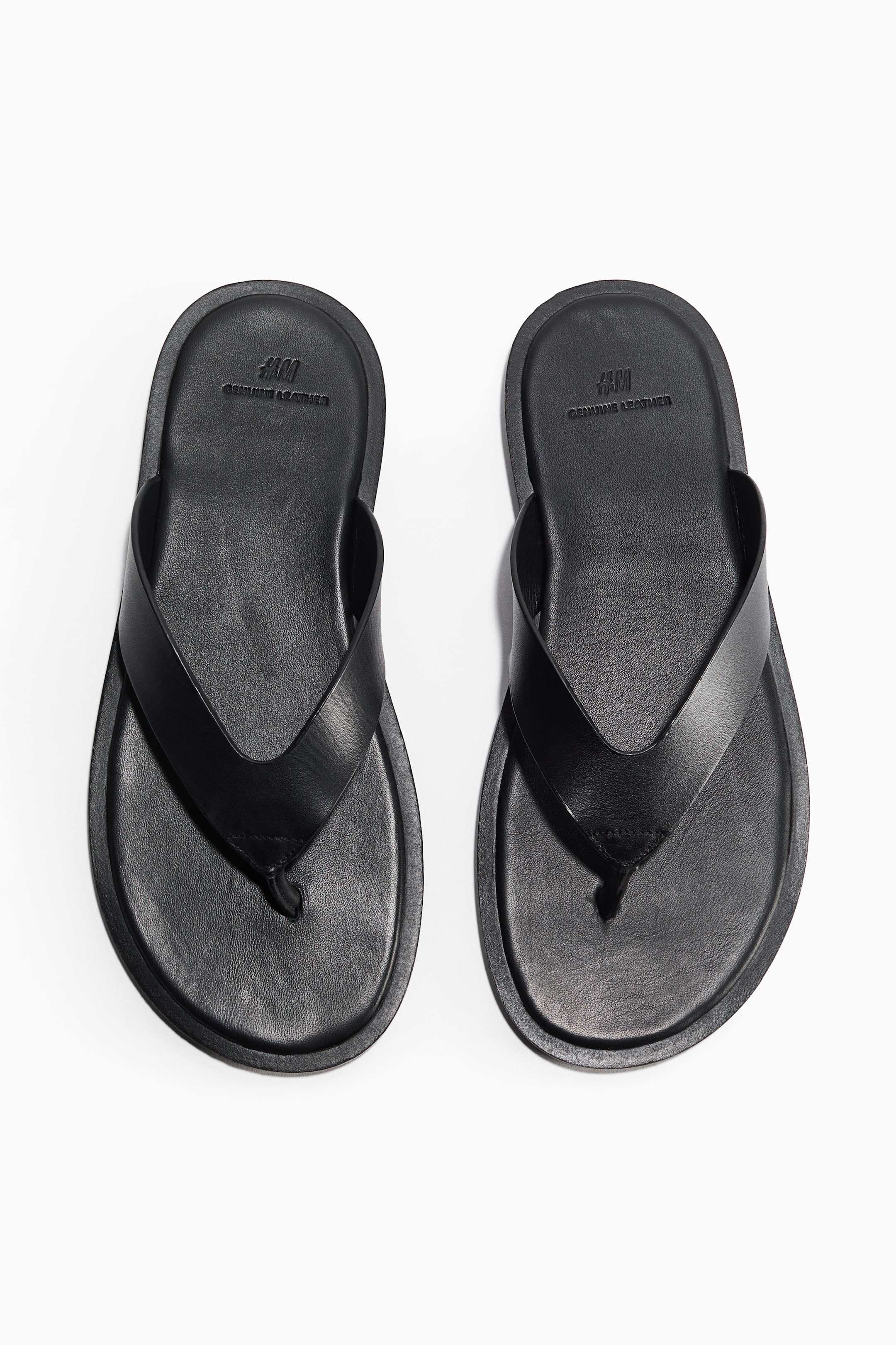 View larger image: Black leather flip-flops are lying flat, featuring round toes, wide straps, and a narrow toe post.