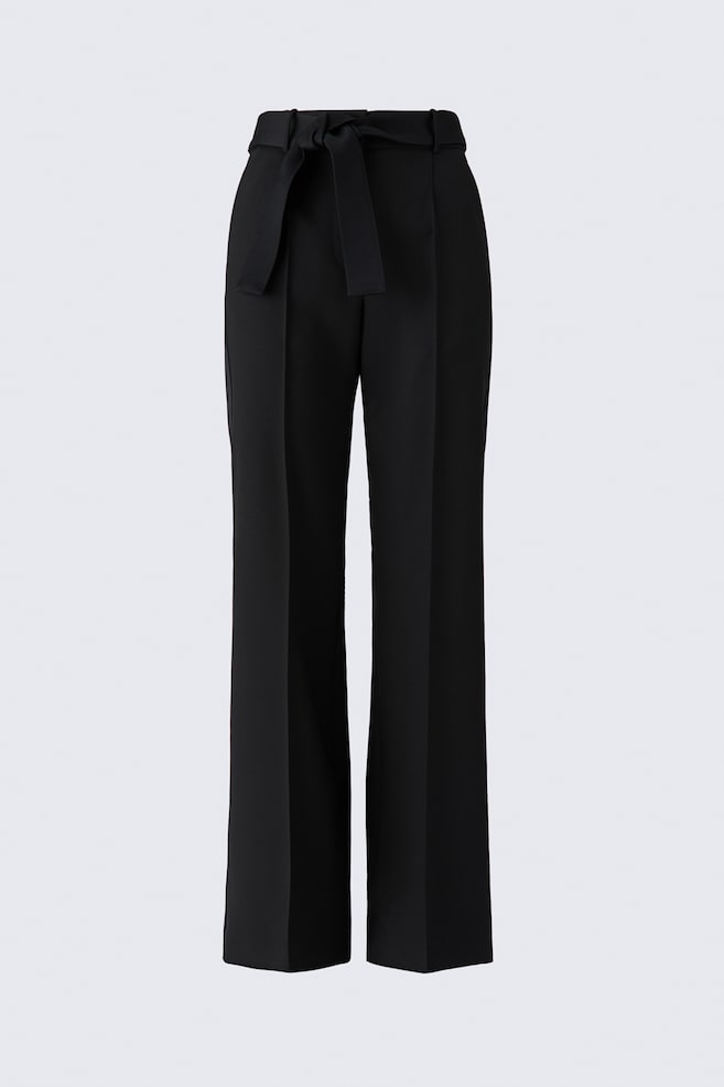 These black tie-detail wool trousers are shown from a front-facing angle, featuring a high-waisted fit with a matching fabric belt knotted at the front. The design is displaying straight, wide legs with sharp pressed creases running down the center of each leg. - 1