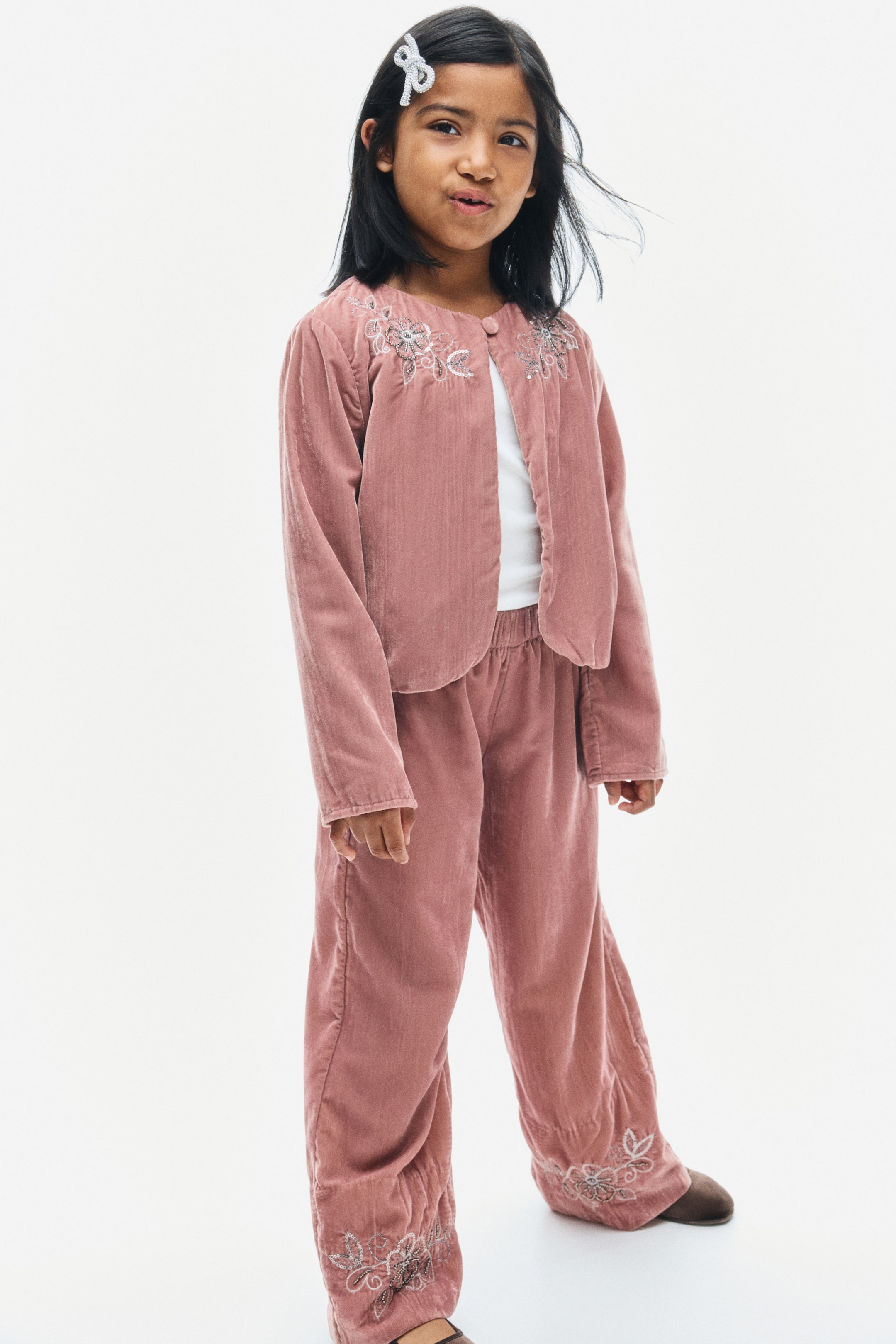 View larger image: Dusty pink velvet pants are shown from the front, featuring an elasticated waist and straight legs. The pants feature intricate floral embroidery at the hems, detailed with beads and sequins.