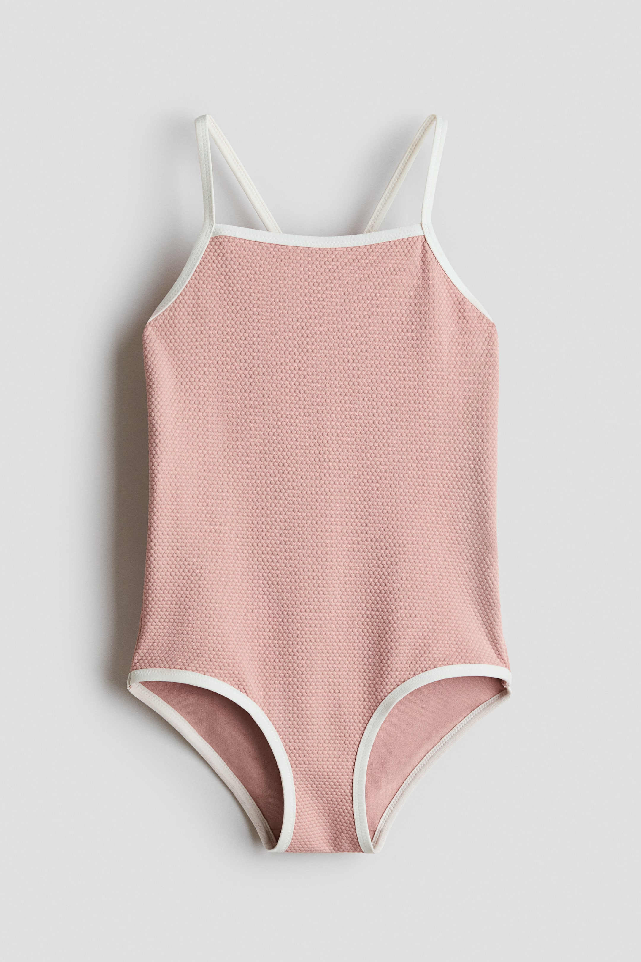View larger image: The H&M Adorables swimsuit is showcased from the front, highlighting its pink textured fabric with a square neckline and narrow shoulder straps that cross at the back. White trim outlines the neckline, armholes, and leg openings.