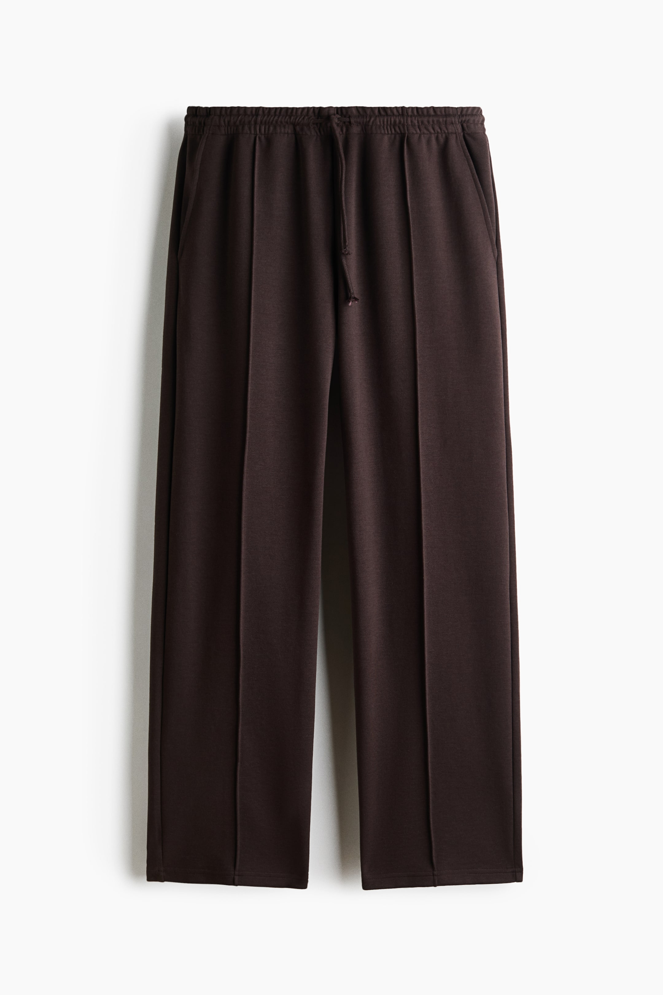 View larger image: Dark brown trousers feature an elasticated waistband with a drawstring, vertical front seams, and side pockets, offering a straight-leg fit.