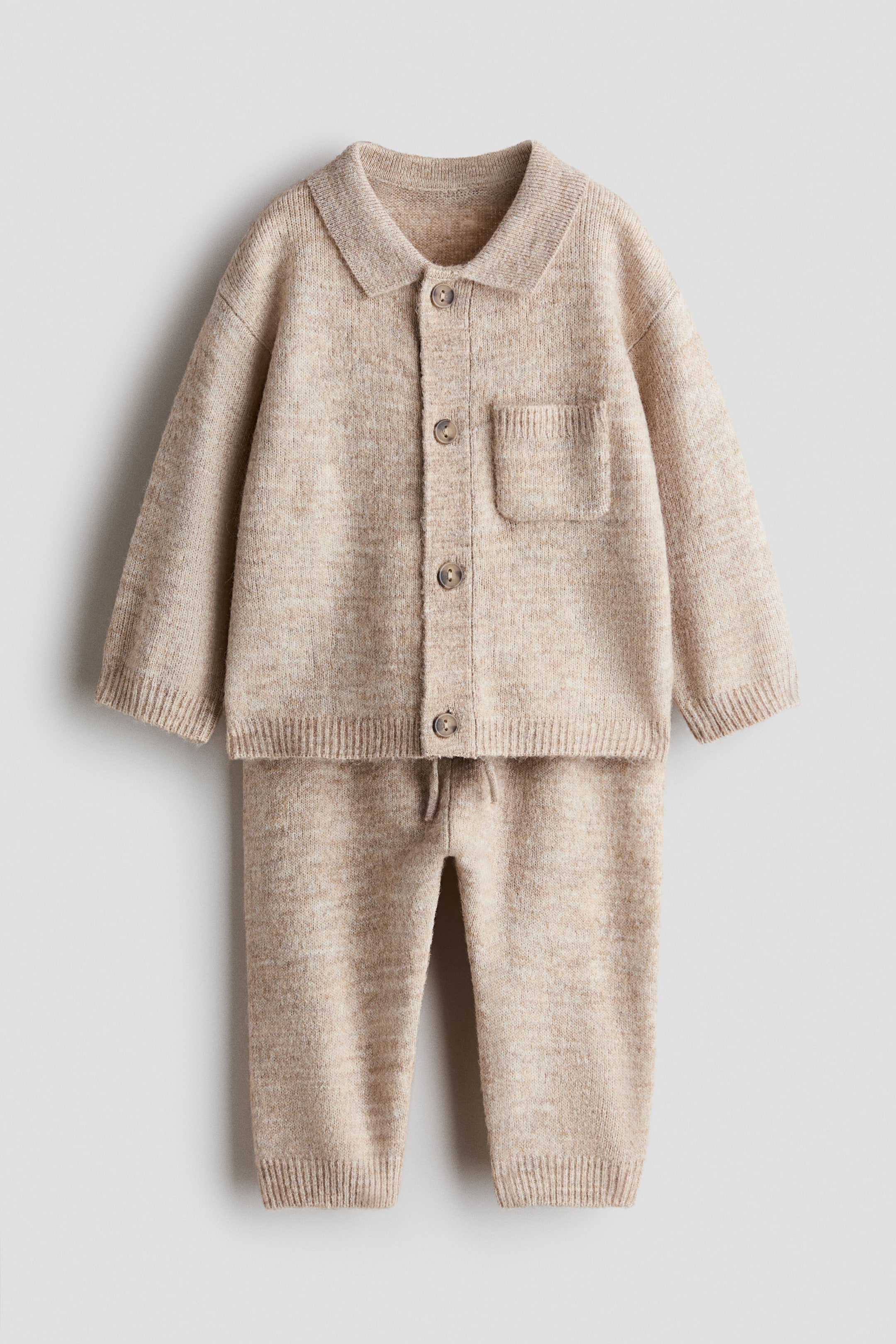 View larger image: A beige melange knit set is shown front-facing, featuring a long-sleeved collared cardigan and matching pants. The cardigan features a button-down front, a single chest pocket, and ribbed cuffs and hem, while the pants feature a drawstring waist and ribbed ankle cuffs.