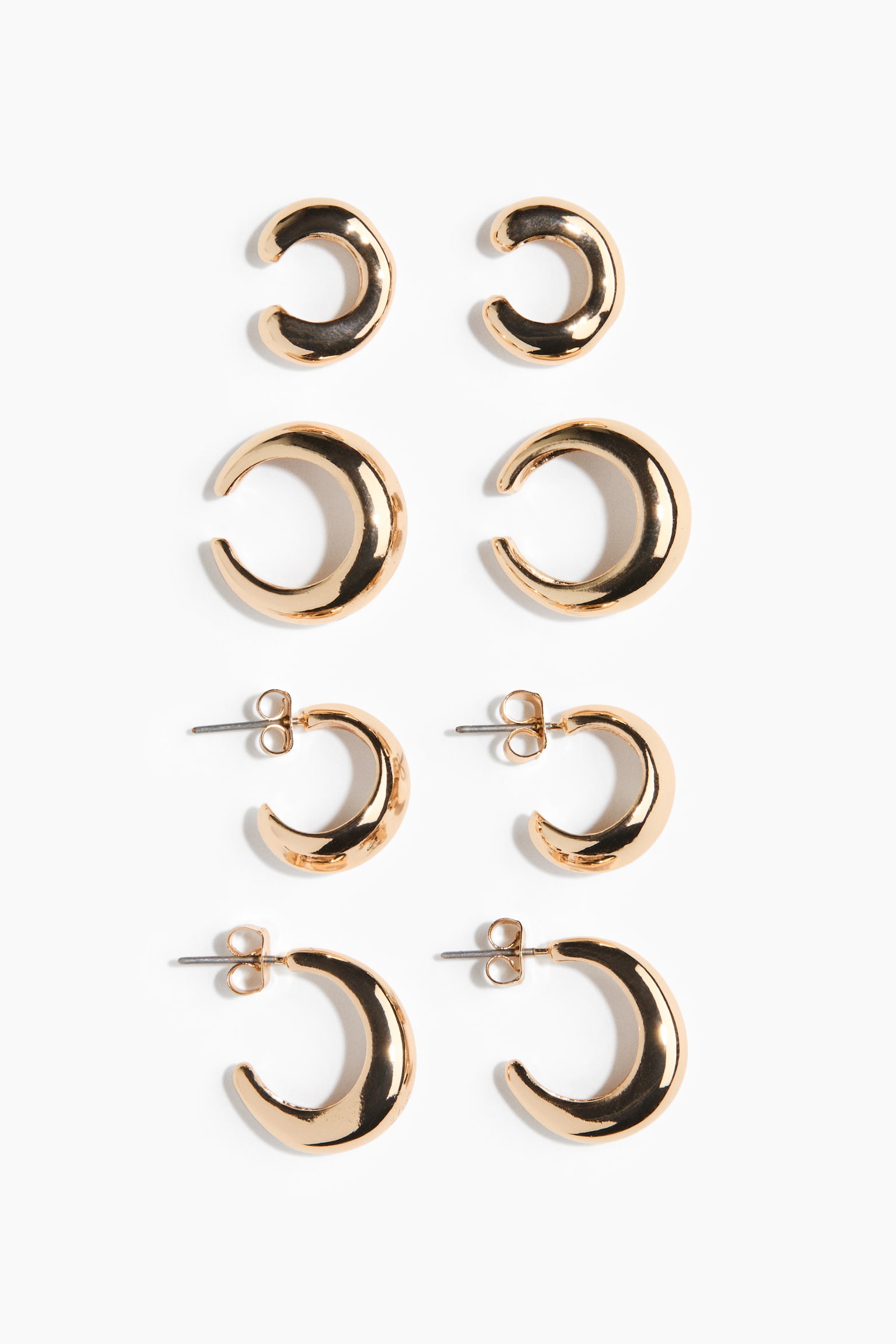 A set of four pairs of gold-toned earrings is displaying a vertical arrangement of polished, crescent-shaped designs. The top two pairs are featuring open-ended ear cuffs in small and medium sizes, while the bottom two pairs are showing hoop earrings with post-back closures and butterfly backings.