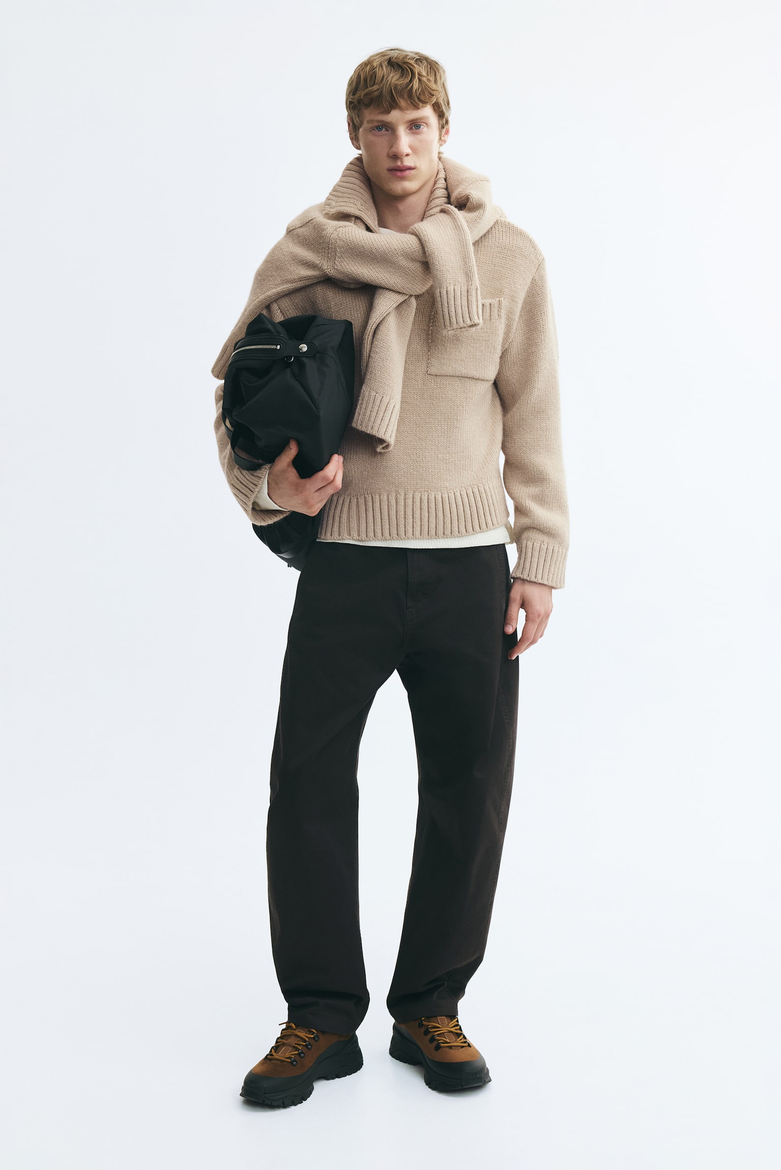 A light beige knit sweater is shown facing forward, highlighting a ribbed collar with an open V-neckline. It features a single patch pocket with ribbed trim on the left chest, long sleeves with wide ribbed cuffs, and a matching ribbed hem. - 1