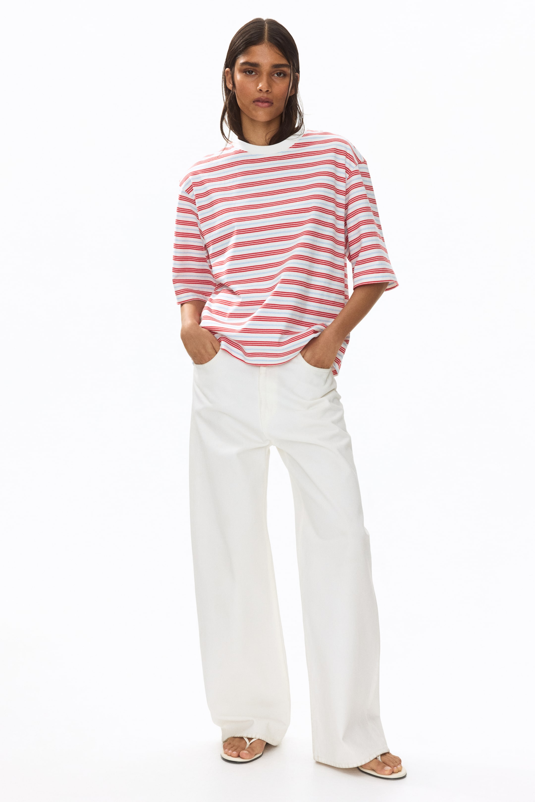 View larger image: The model is showcasing an oversized t-shirt adorned with horizontal stripes in white, red, and light blue. This t-shirt, designed in a boxy style, comes with a round, rib-trimmed neckline, dropped shoulders, elbow-length sleeves, and a straight-cut hem. The model is posed with hands tucked into the pockets of white trousers.