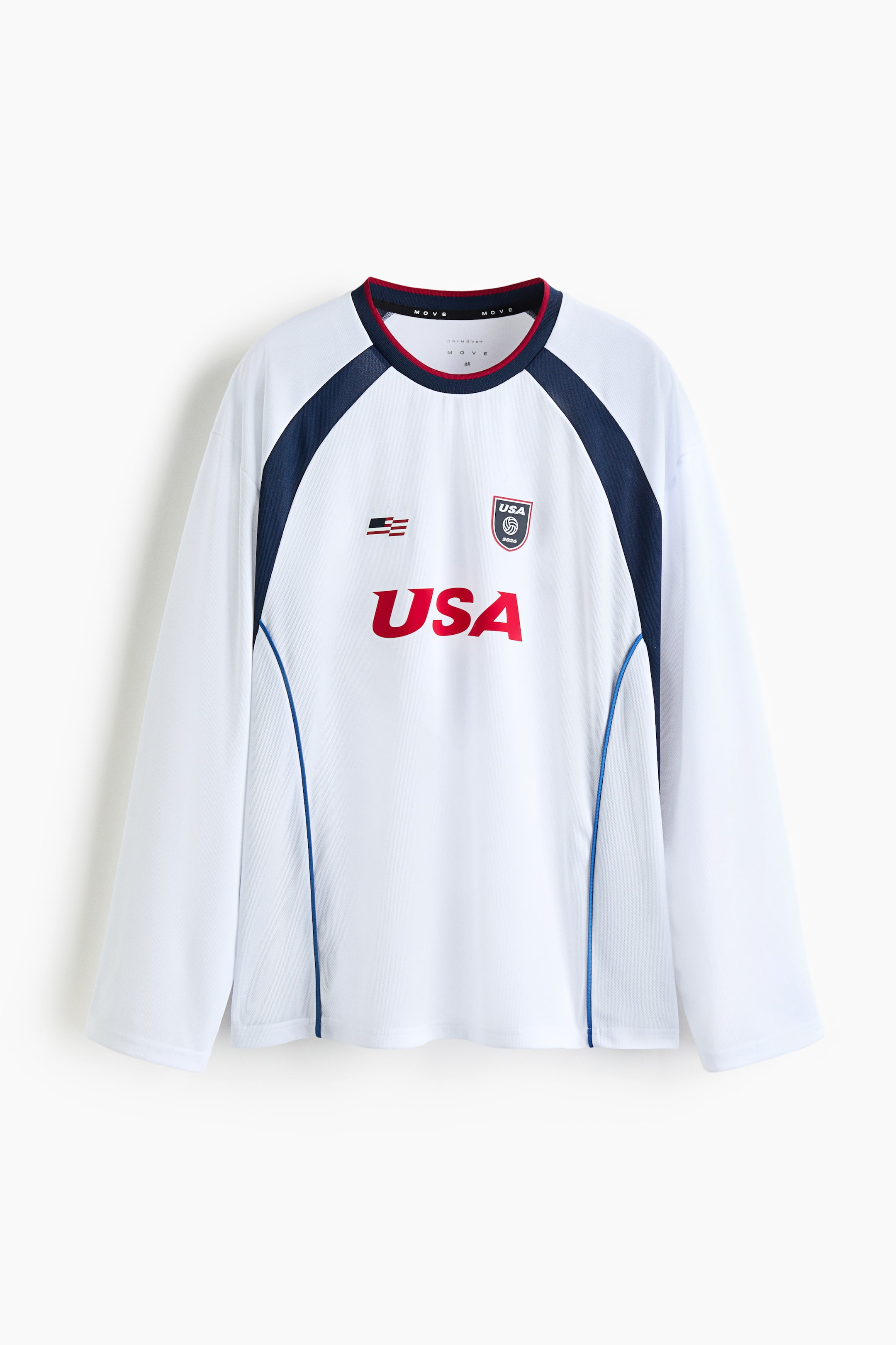 View larger image: A white long-sleeve shirt featuring a subtle textured fabric, a red and blue trimmed crew neck, and dark blue raglan panels extending over the shoulders and down the sides, accented with blue piping. The front displays "USA" in bold red letters, an embroidered USA crest, and a flag emblem.