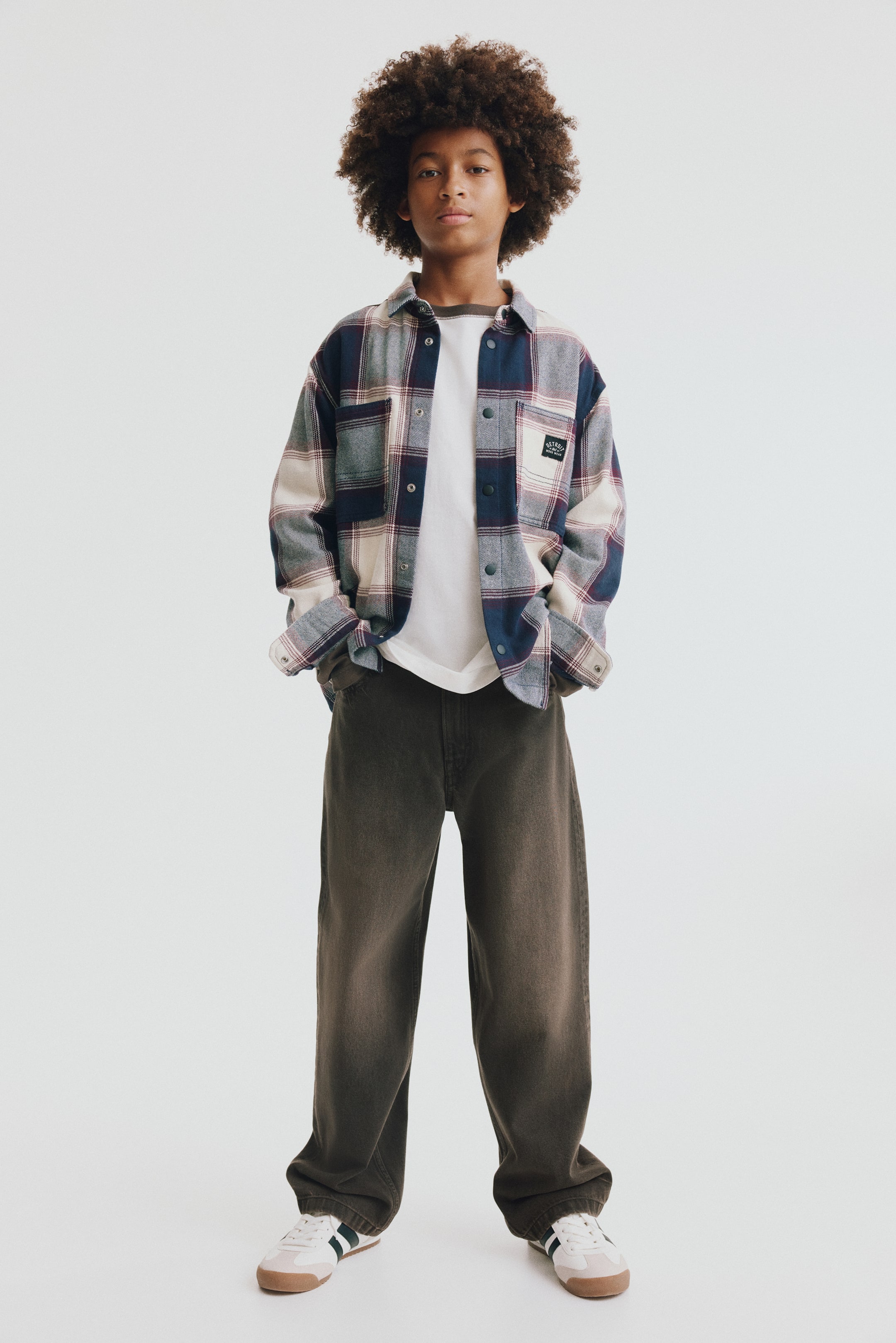 Agrandir l'image: Jean en denim délavé coupe loose, dans un gris-brun foncé délavé, vu de face, avec une coupe ample à jambe large et entrejambe bas. Le bas du jean tombe légèrement sur les sneakers, mettant en valeur sa coupe décontractée au niveau des hanches et des cuisses.