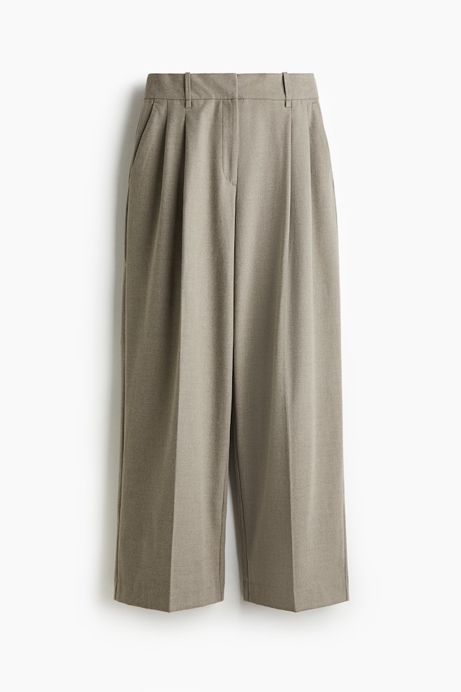 VORNE, eine locker sitzende, maßgeschneiderte Hose aus gewebtem Stoff, zeigt eine hohe Taille mit Reißverschluss und verdeckten Knopf- und Hakenverschlüssen. Diagonale Seitentaschen sind sichtbar, und die weiten Beine weisen oben Falten und vorne verlaufende Bügelfalten auf. - 1