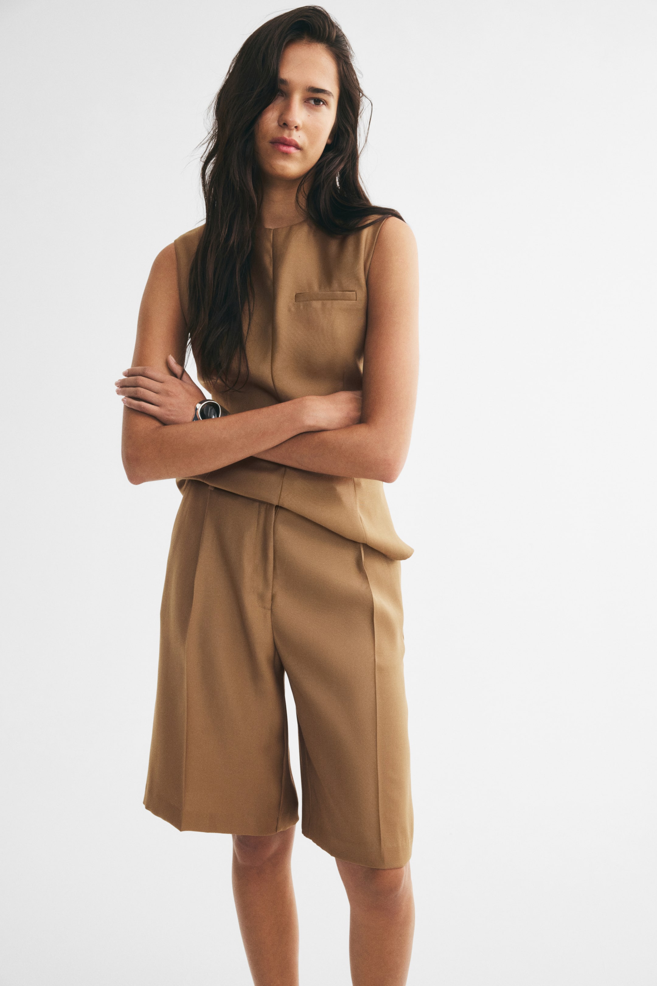View larger image: The model is wearing knee-length tailored shorts in a camel-colored basket weave, featuring a high waist, front pleats, and pressed creases down the front. The shorts are styled with a matching sleeveless top.